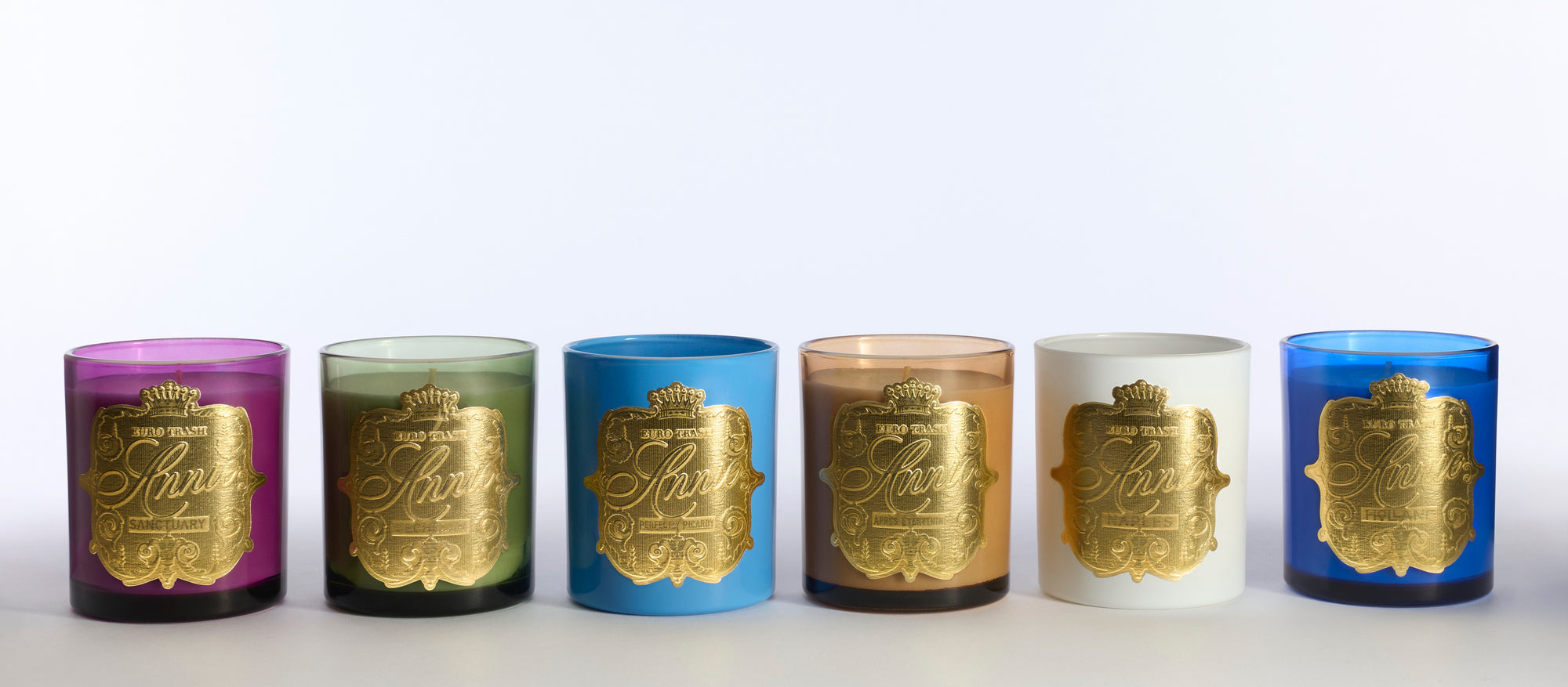 Naples includes six decorative scented soy candles in colorful glass holders—purple, green, light blue, dark blue, amber, and white—with ornate gold labels. Clean-burning and floral-scented, they make a stunning display when arranged in a row.
