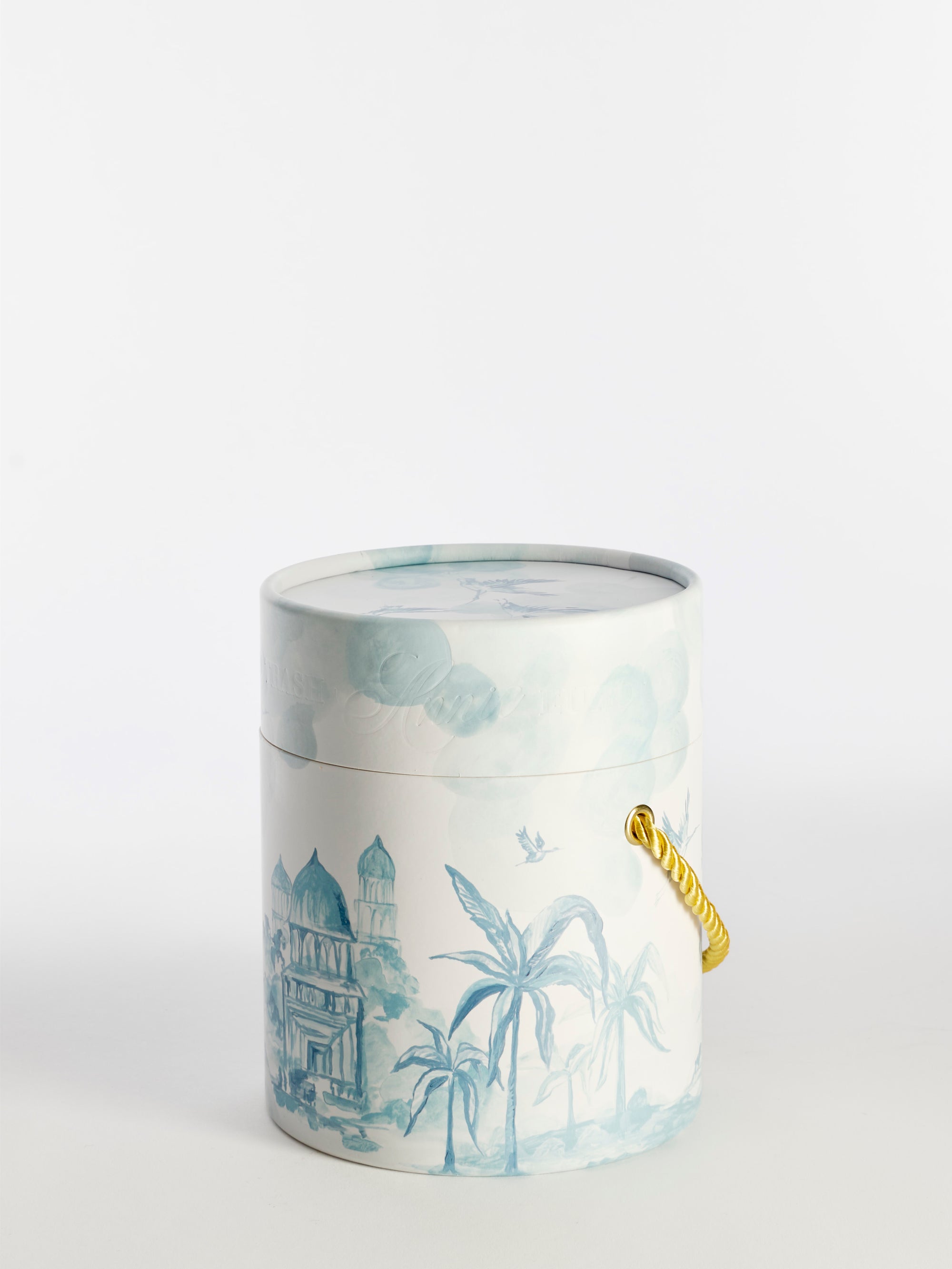 Perfectly Picardy is a cylindrical, phthalate-free floral candle in a lidded container with light blue domed buildings and palm trees, a gold-colored rope handle, and photographed against a plain white background.