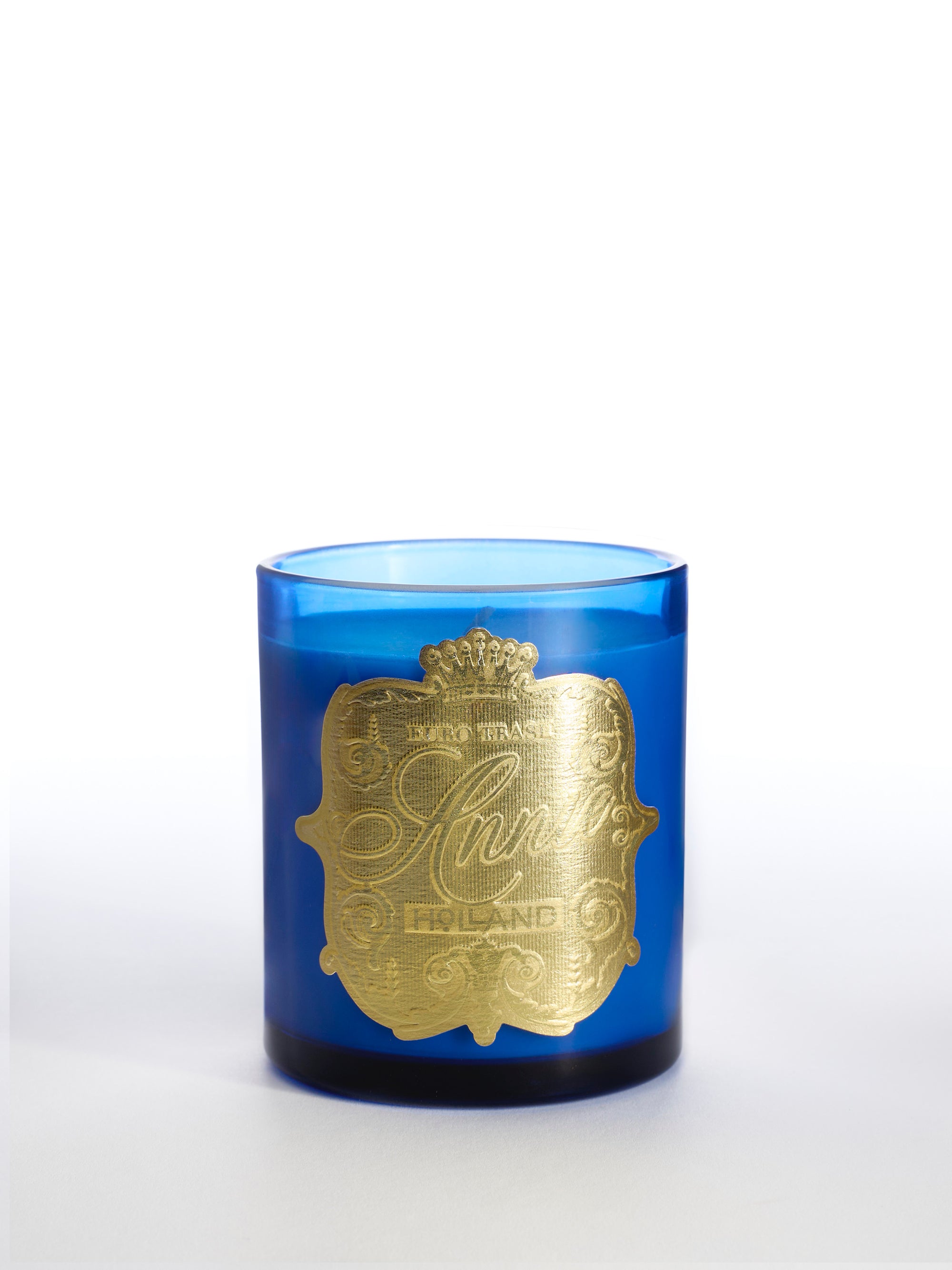 The Holland candle holder is a blue glass piece with an ornate gold label, decorative text, and a crown design—ideal for displaying a luxurious oud mahogany candle against a white background.