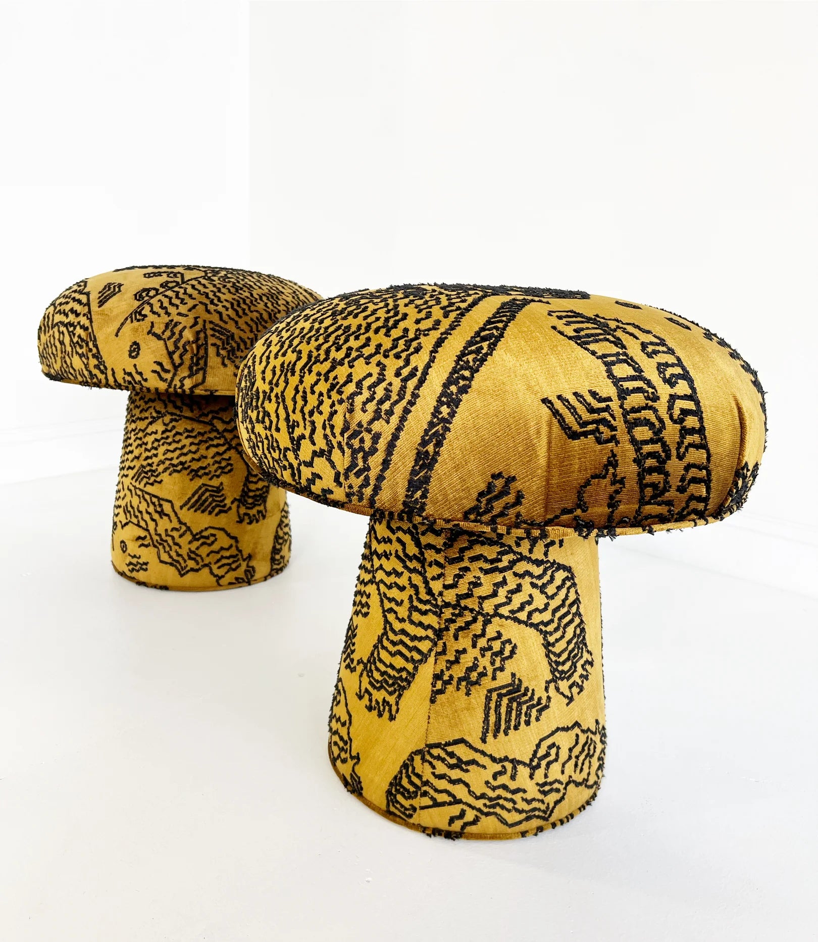 Two Forsyth Mushroom Poufs in Dedar 'Tiger Mountain' jacquard velvet, with yellow upholstery and abstract black lines, are placed on a white floor against a plain white background.