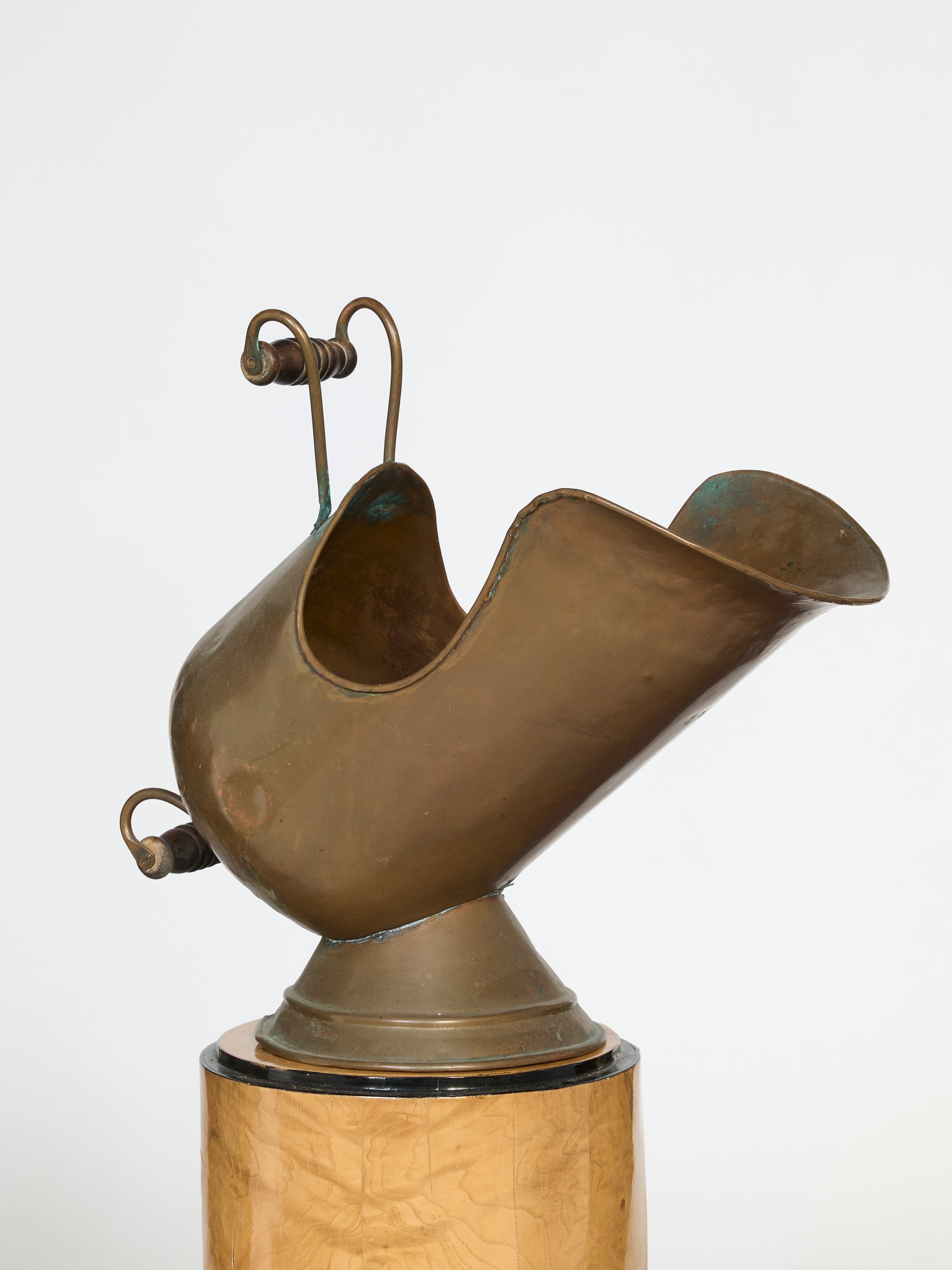 The Hand-Forged Brass Coal Scuttle Vessel features a curved handle and spout, standing upright on a round wooden base. This solid brass decor piece adds elegance to any space, highlighted here against a plain white background.