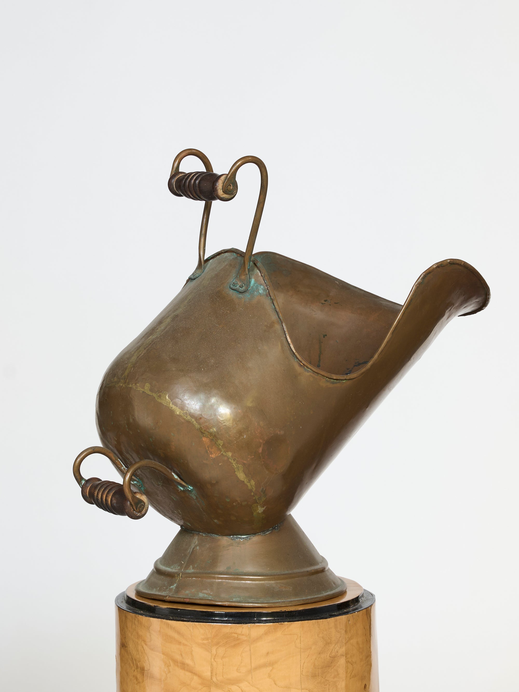 A bronze abstract sculpture with curved, organic shapes and two upward handles evokes the Hand-Forged Brass Coal Scuttle Vessel, mounted on a circular wooden base against a plain white background.