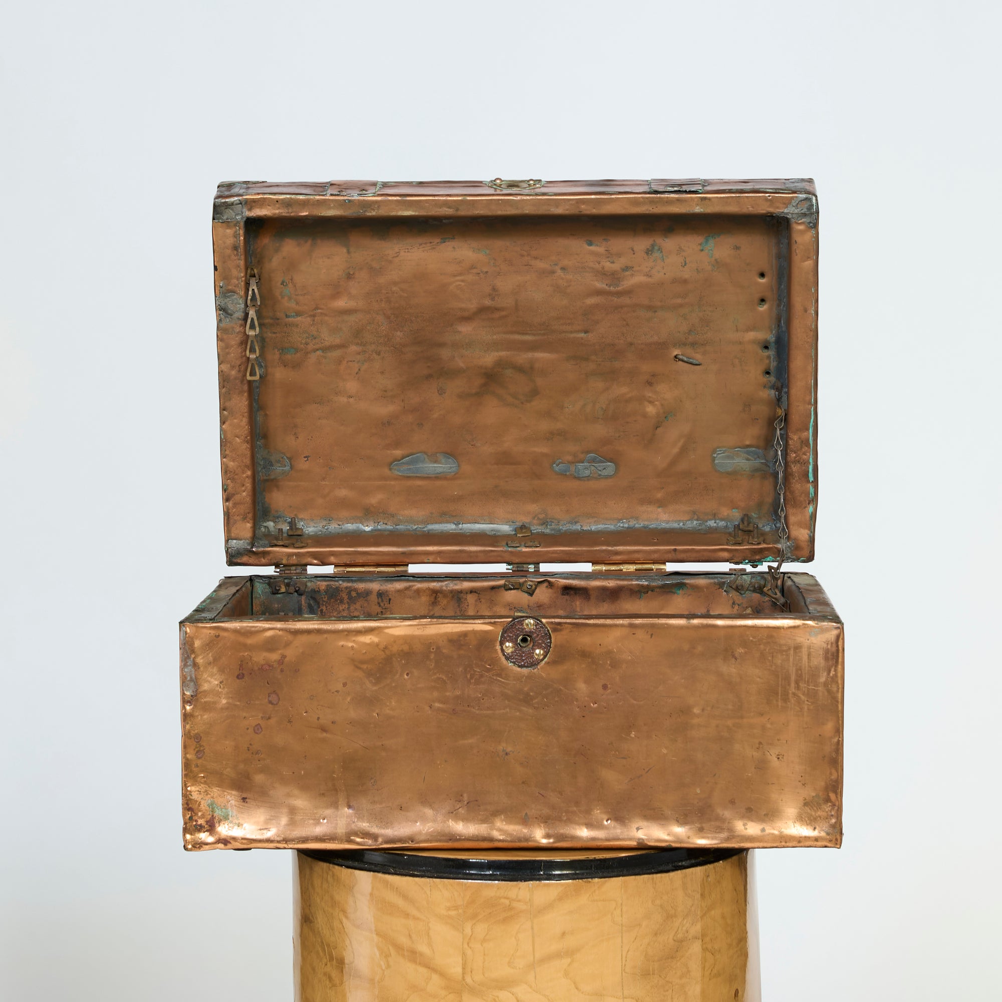 The Antique Copper-Clad Trunk, a weathered handcrafted storage box with an open hinged lid, sits on a decorative pedestal, its empty interior visible against a plain light background.