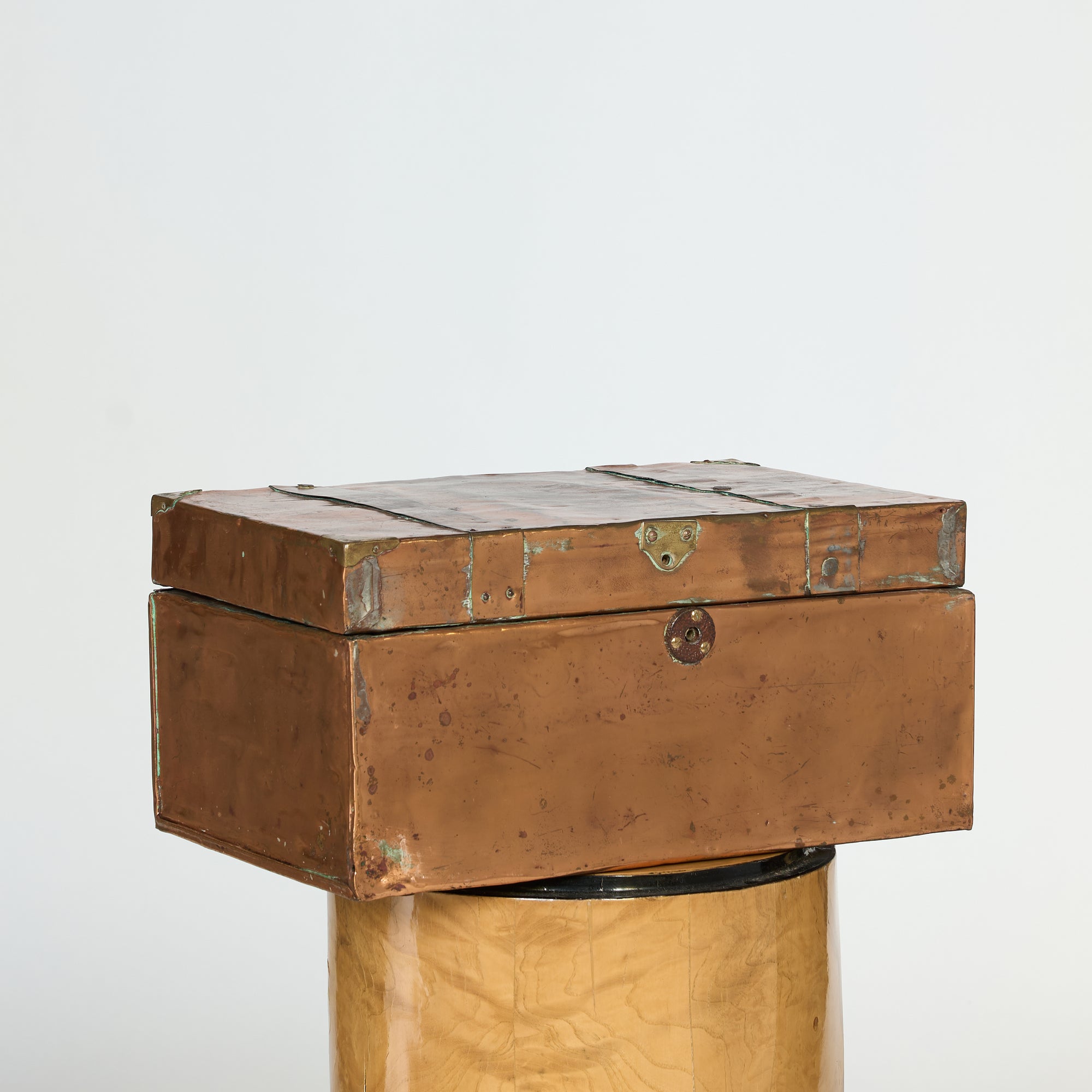 The Antique Copper-Clad Trunk, a rectangular handcrafted storage box with metal fittings and latch, sits on a decorative pedestal, its vintage charm accentuated against a plain white background.