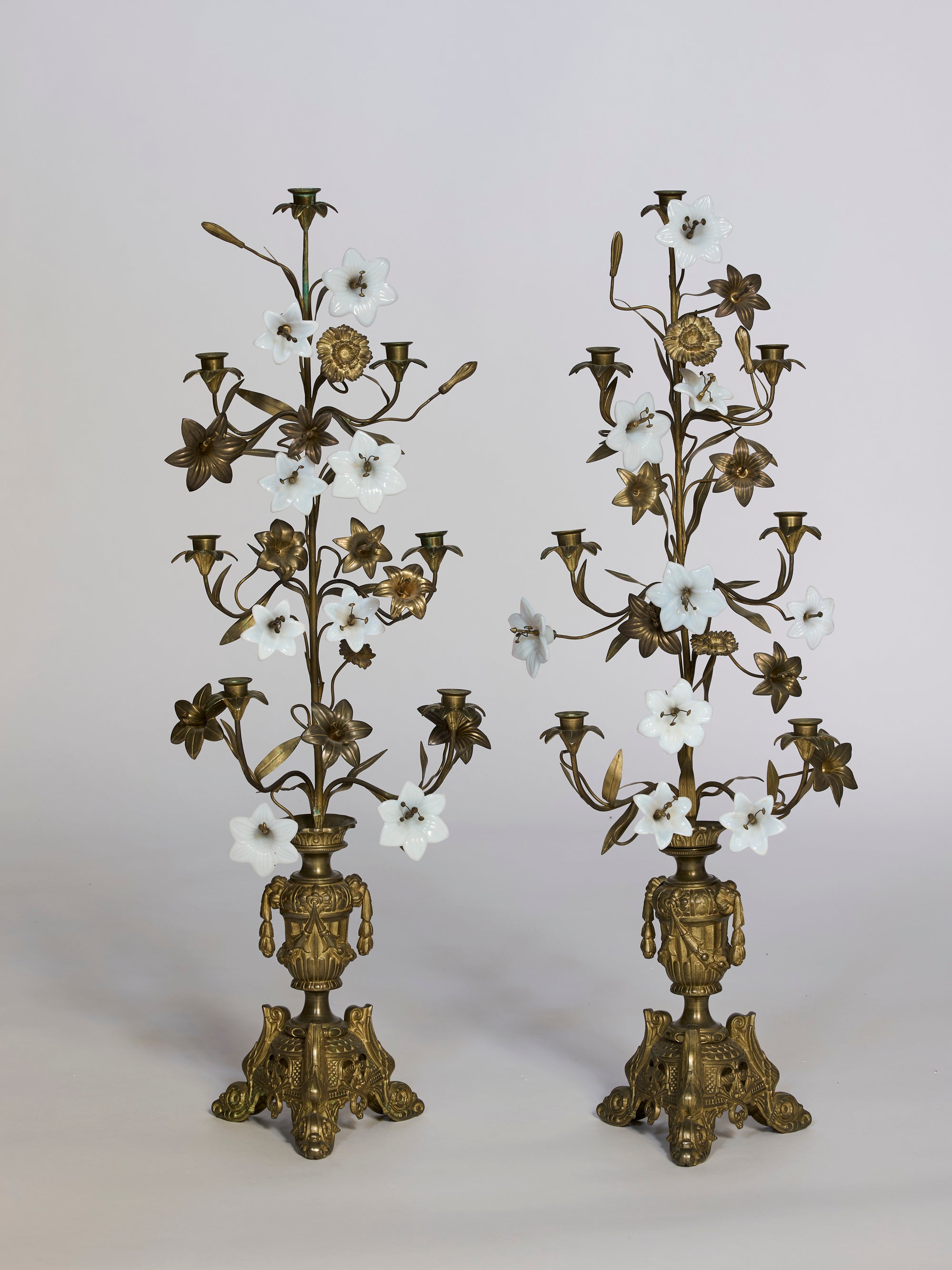 The Gilded Floral Candelabra Pair with Opaline Blossoms features ornate gilt bronze, intricate floral designs, and white opaline glass flower accents, each with multiple holders on elaborate decorative bases.