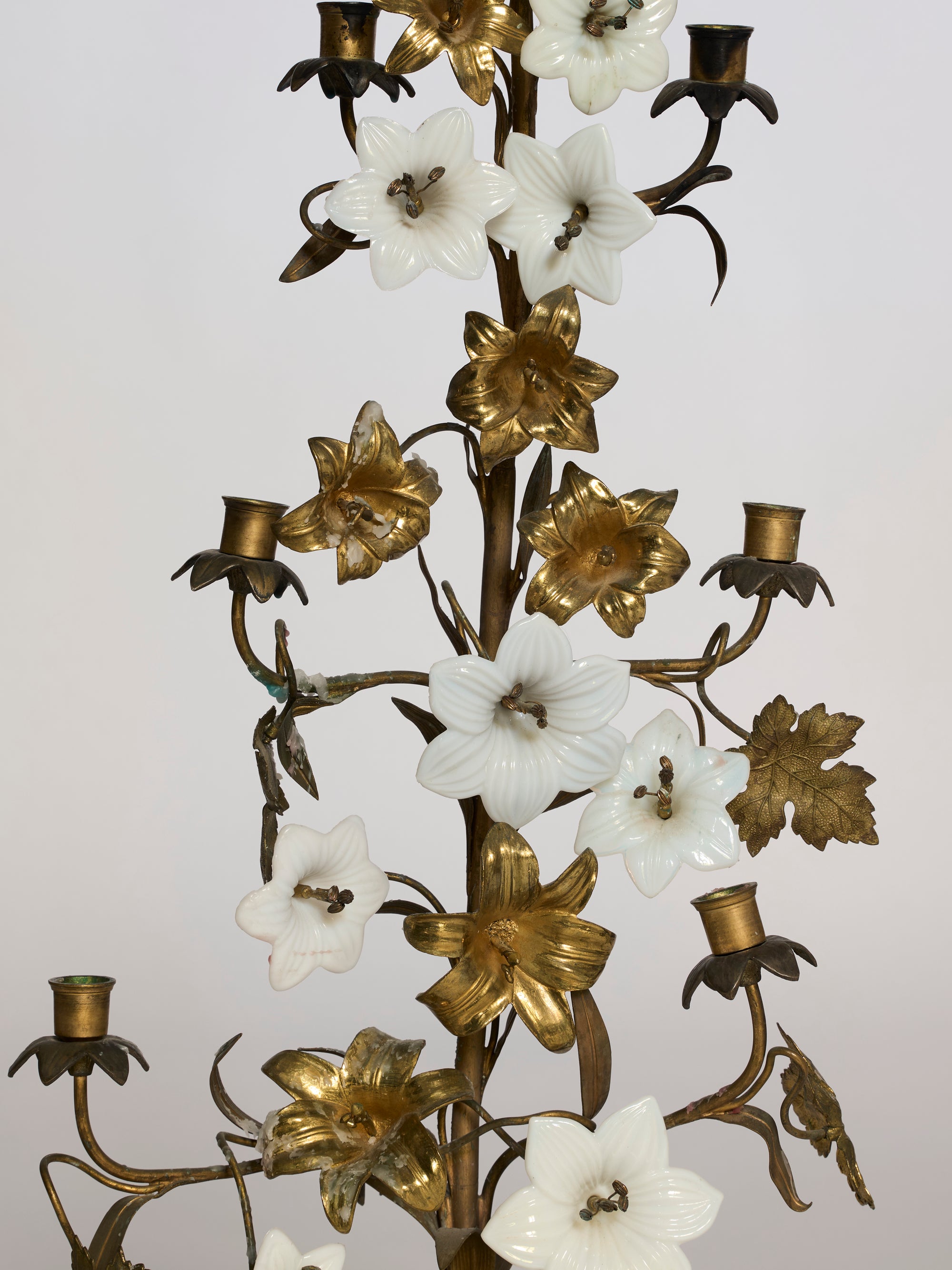 The Pair of Floral Brass Candelabra Sculptures showcases gold leaves and branches with white and gold flower accents, featuring empty candle holders elegantly arranged among the decorative blooms.