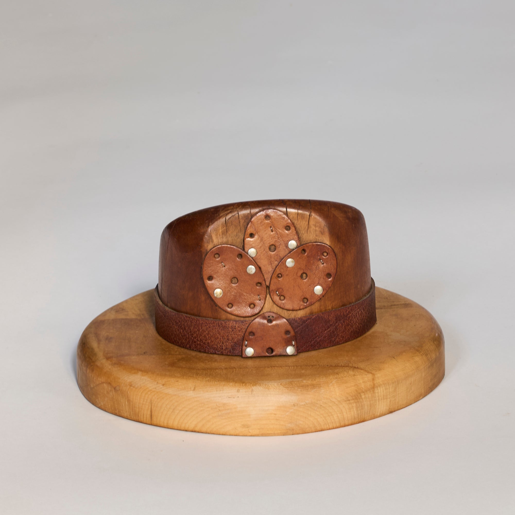 An Antique Wooden Millinery Hat Mold is displayed as a collectible on a round wooden stand against a plain light background.