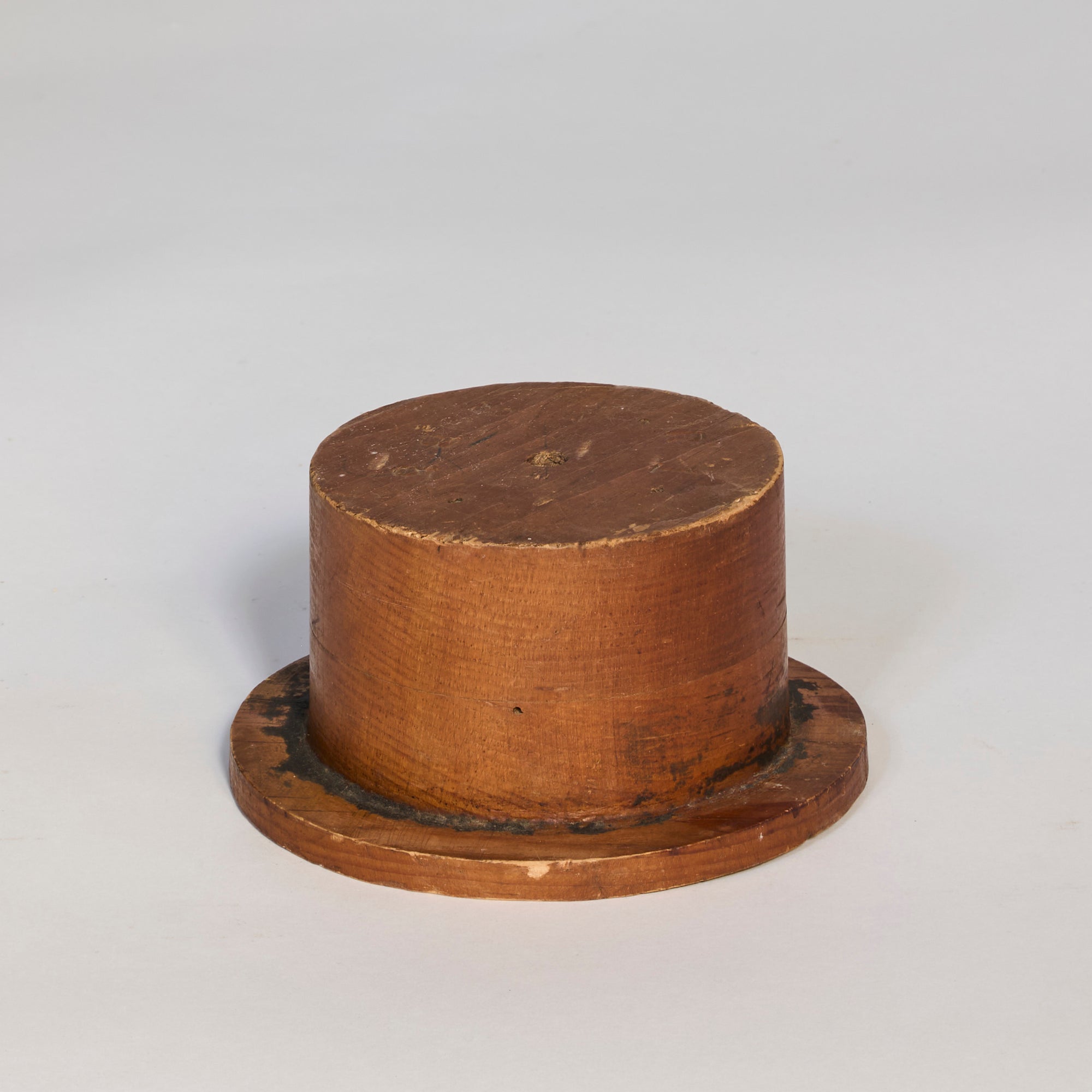 The Antique Wooden Hat Mold is a round, wooden decorative object with a flat base and cylindrical shape, resembling a short, wide drum, displayed on a plain light surface as a unique interior accent piece.
