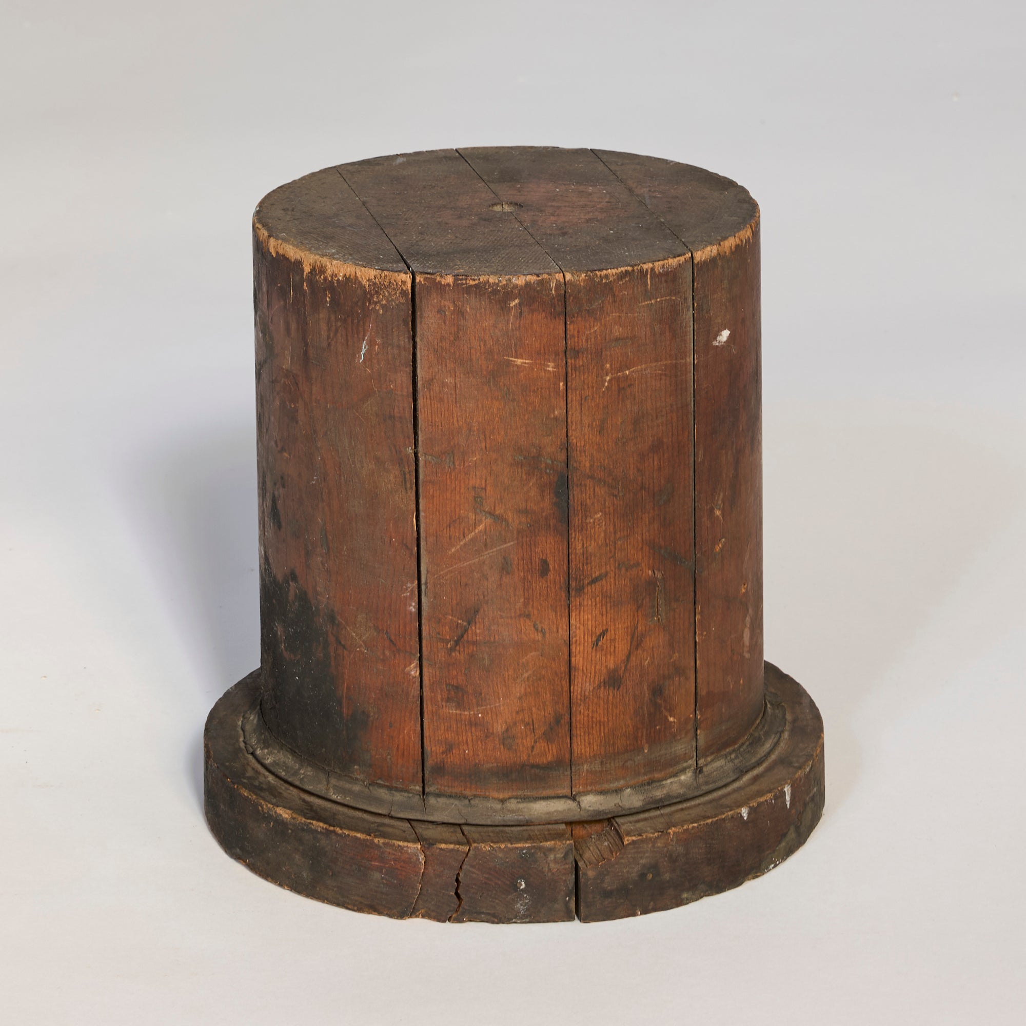 The Antique Wooden Industrial Form is a cylindrical object with a flat top and base, featuring visible cracks and wear. Its dark brown, weathered wood makes it a distinctive collectible ideal for designers seeking vintage appeal.