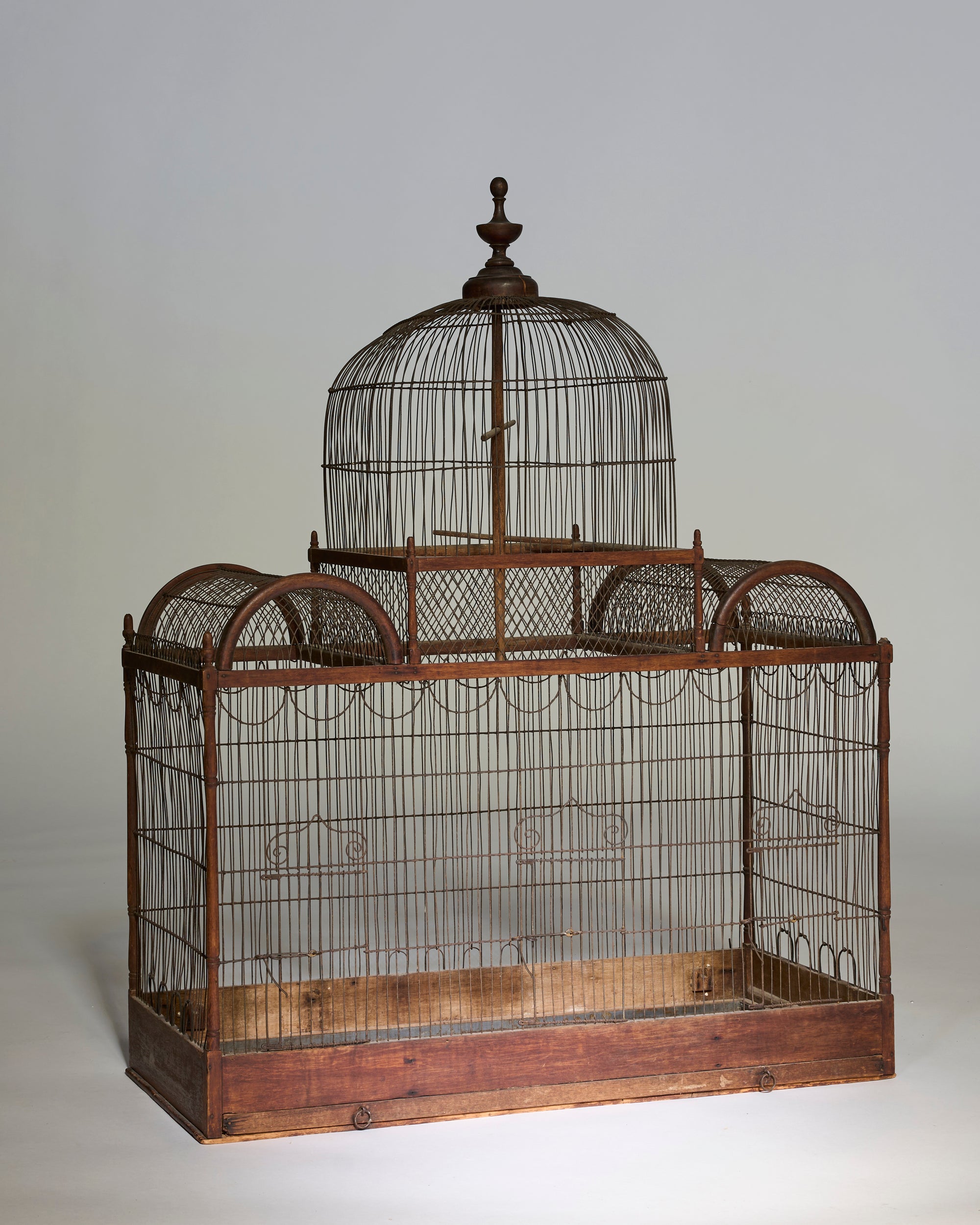 The Antique Architectural Wooden Birdcage Structure features thin metal wires, a large central dome with two smaller domes on each side, and rests on an antique wooden base against a plain background.
