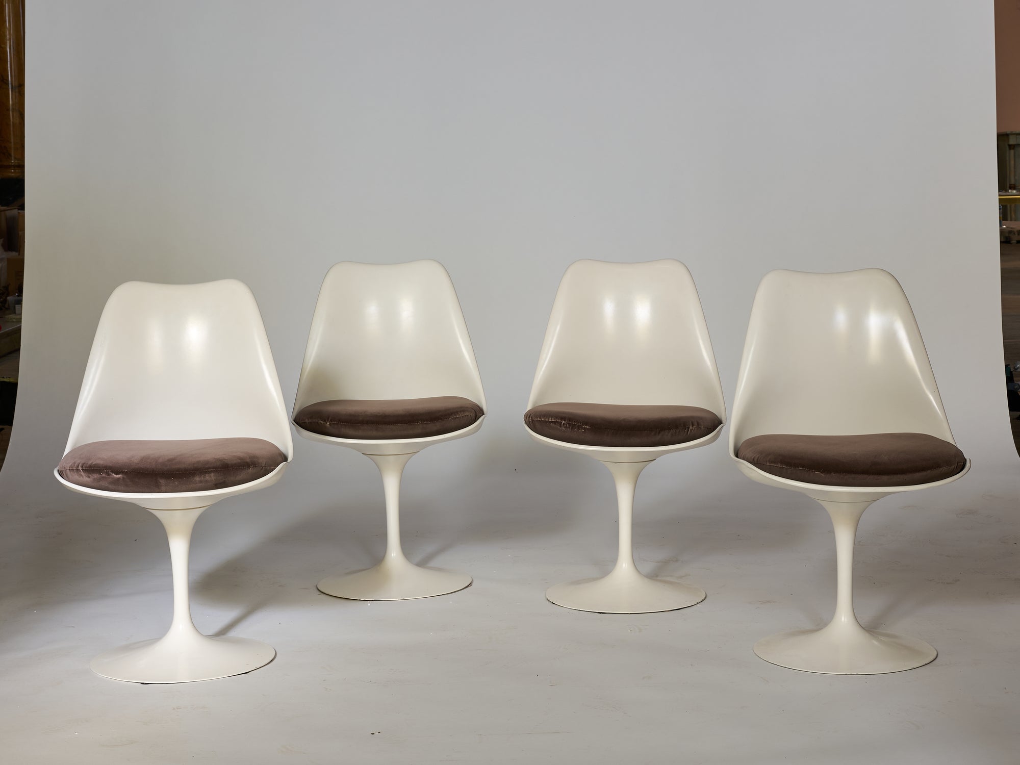 Four Vintage Mid-Century Modern Tulip Chairs with brown cushioned seats are arranged in a row against a plain, light-colored backdrop.