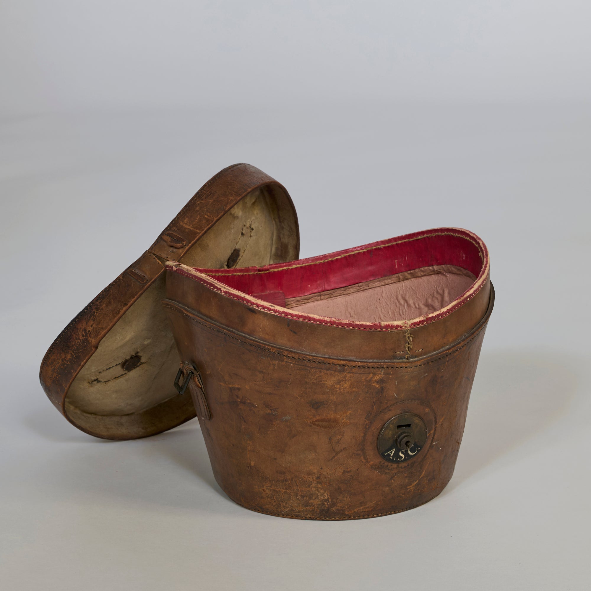 The Antique Leather Storage Case is boat-shaped and brown with an open lid showing a pink-lined interior. Its exterior has a circular black ASC patch. This decorative item rests on a light grey surface.