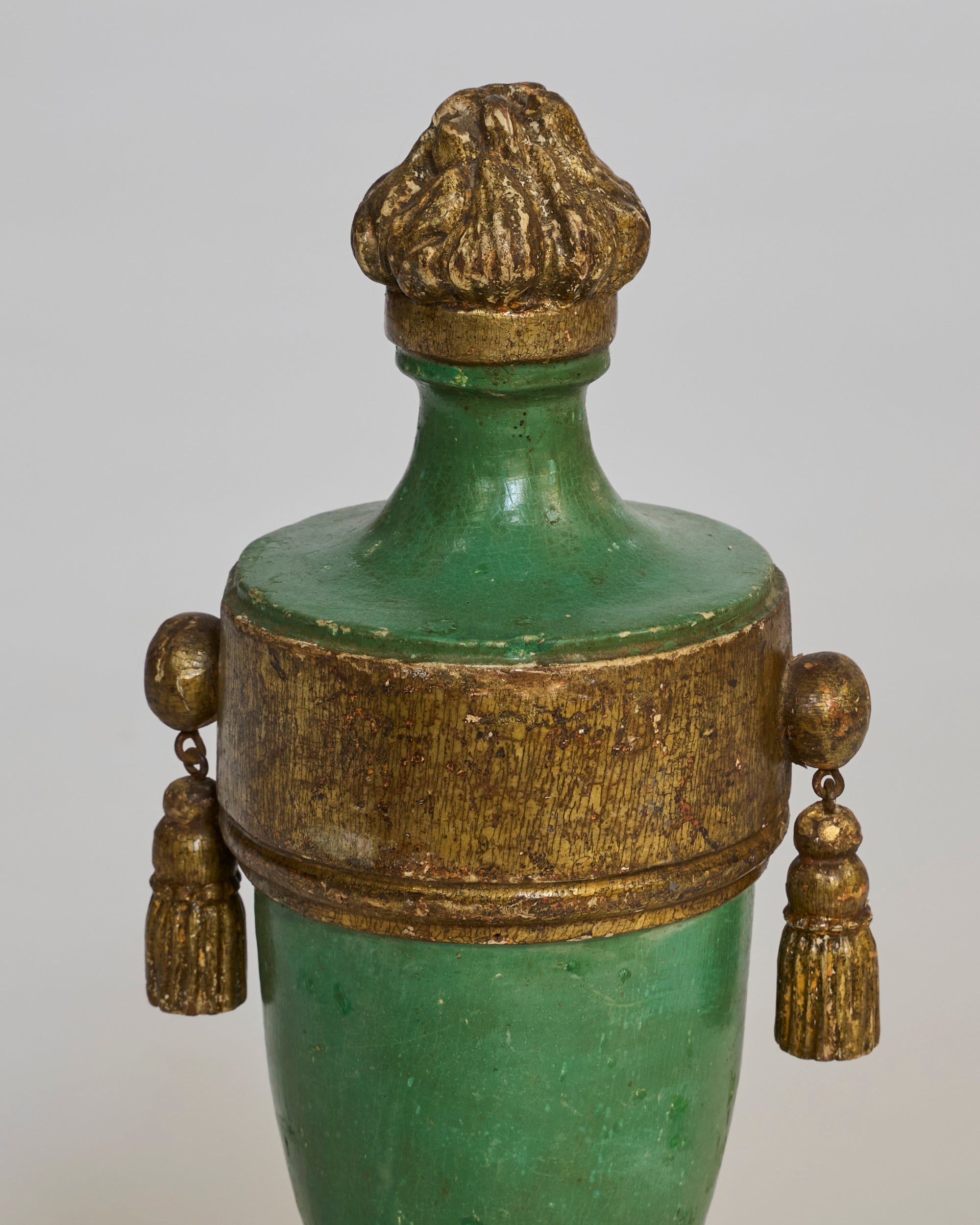 The Pair of Antique Style Green & Gilt Urns feature a classic European-inspired design with gold-painted rims, finials, and two gold tassel ornaments on each side. Shown against a plain light background.