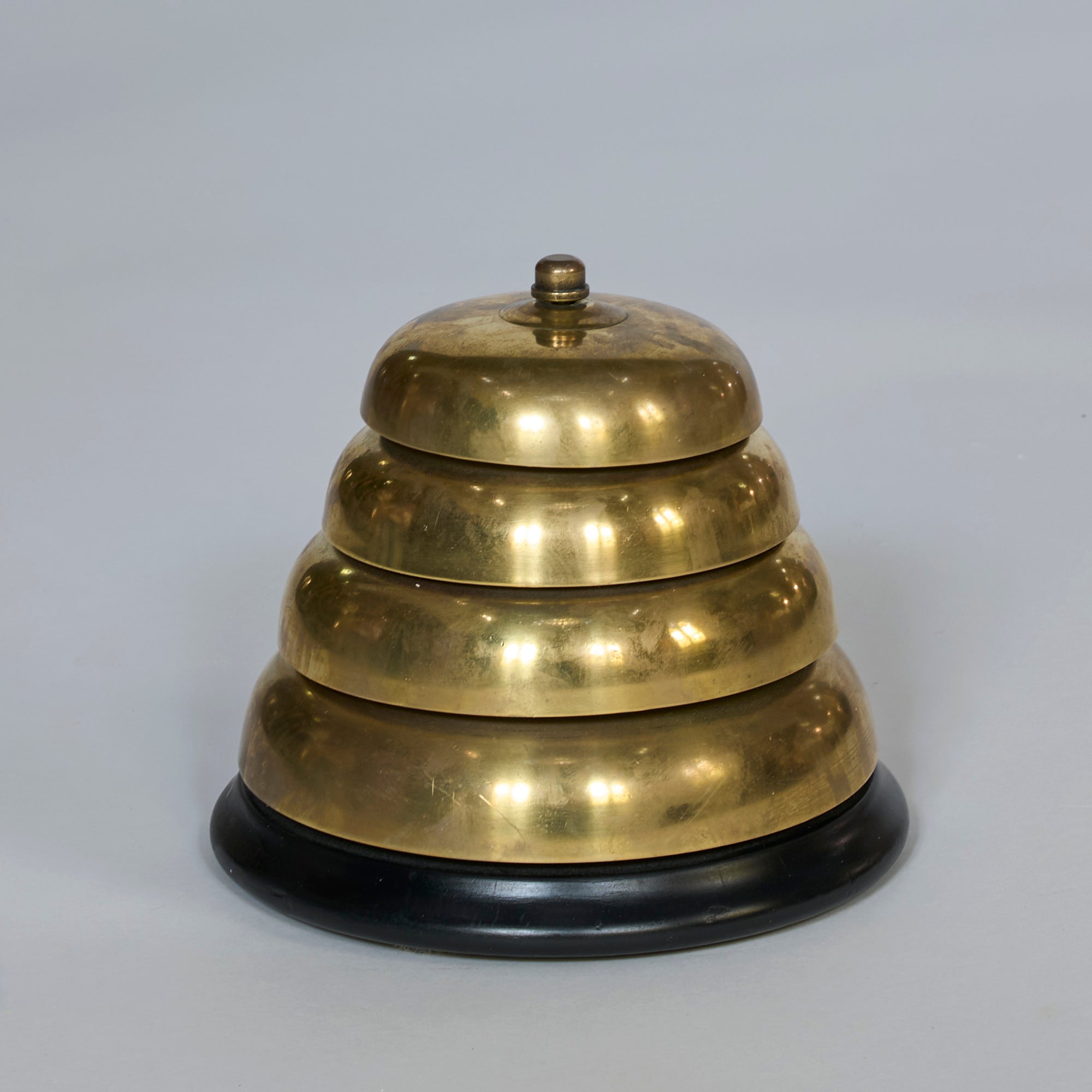 The Vintage Brass Service Bell with Black Base features three stacked, dome-shaped tiers and a small top knob, creating an ideal decorative accent against a plain light background.