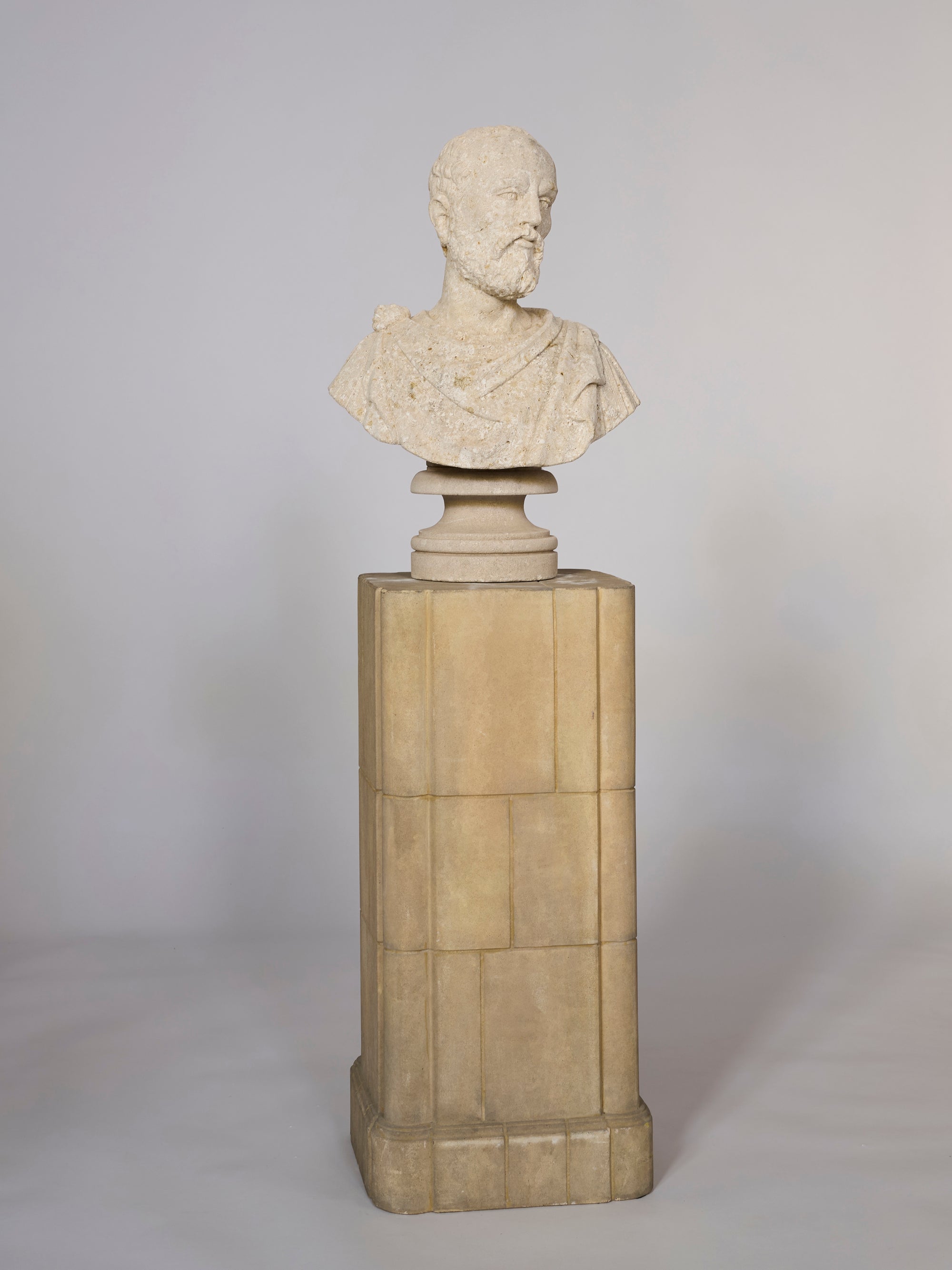 The Classical Style Coral Bust of a Bearded Philosopher is displayed on a tall, rectangular pedestal against a plain, light-colored background.