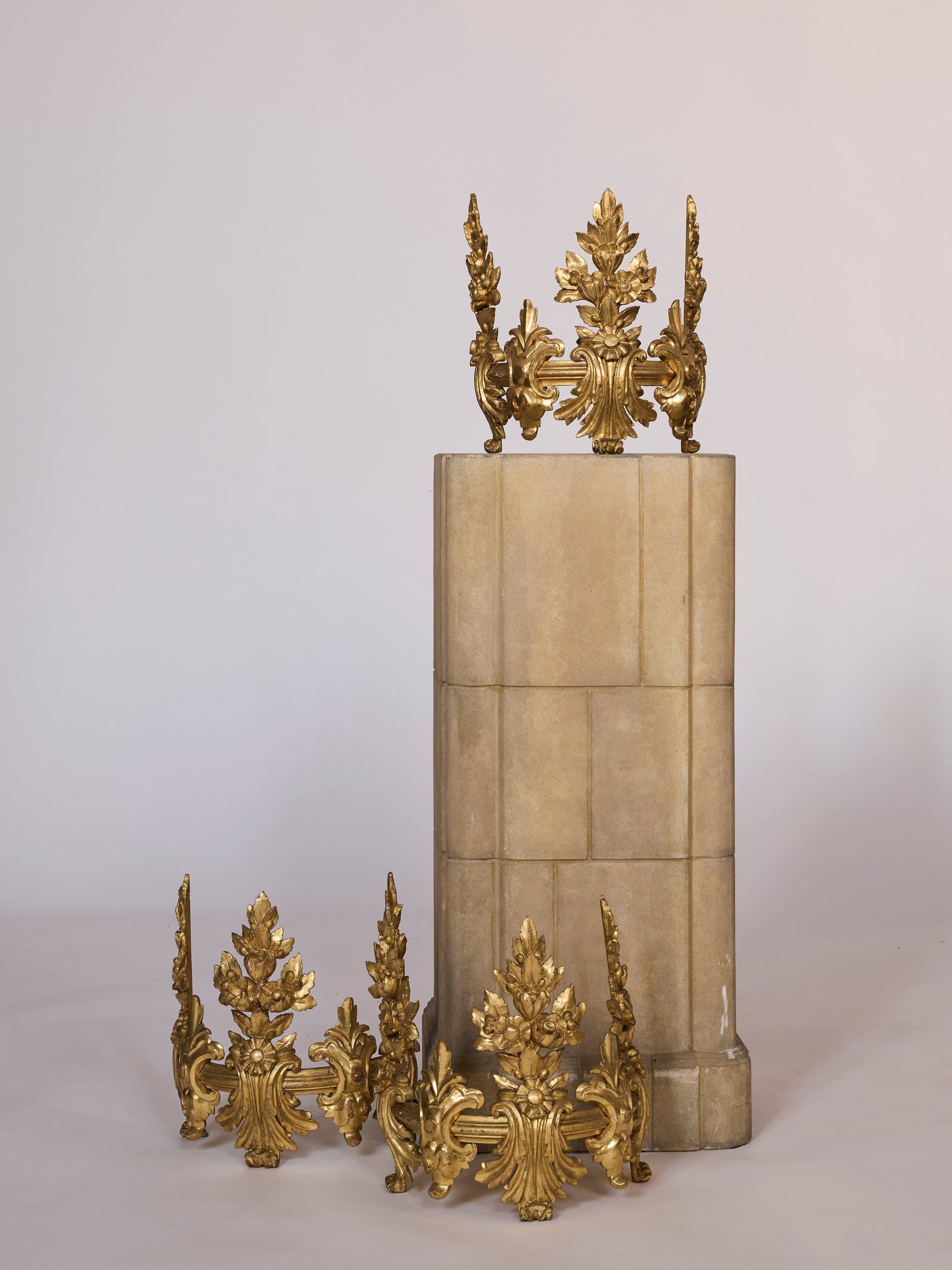 Three Gilt Bronze Architectural Ornaments with leaf and floral designs are displayed: two on the floor and one on a beige stone pedestal, exemplifying striking French water gilt style in classical European decor.