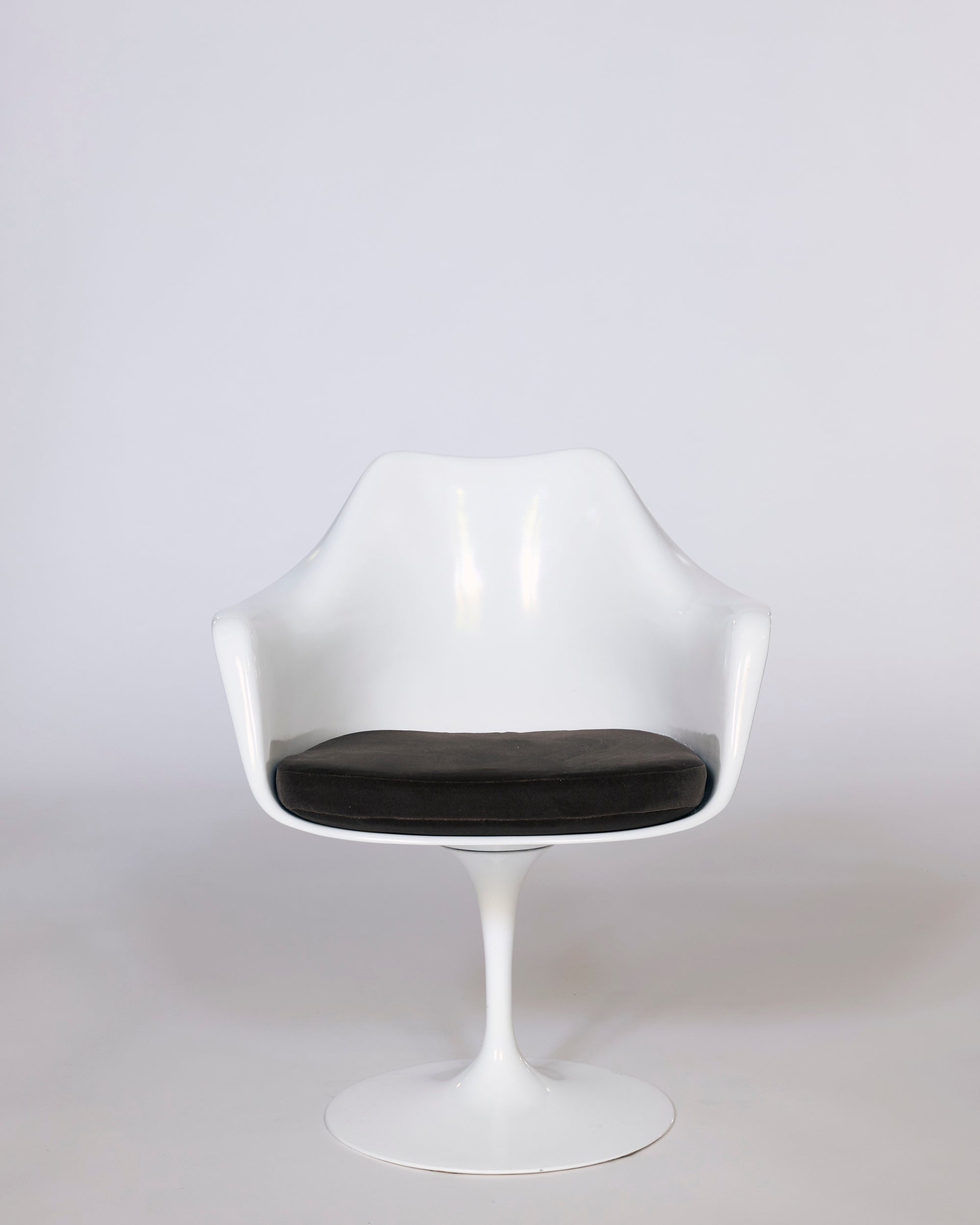 The Mid-Century Tulip Armchair features a molded white shell with curved armrests and a round black cushioned seat, displayed against a plain light gray background.