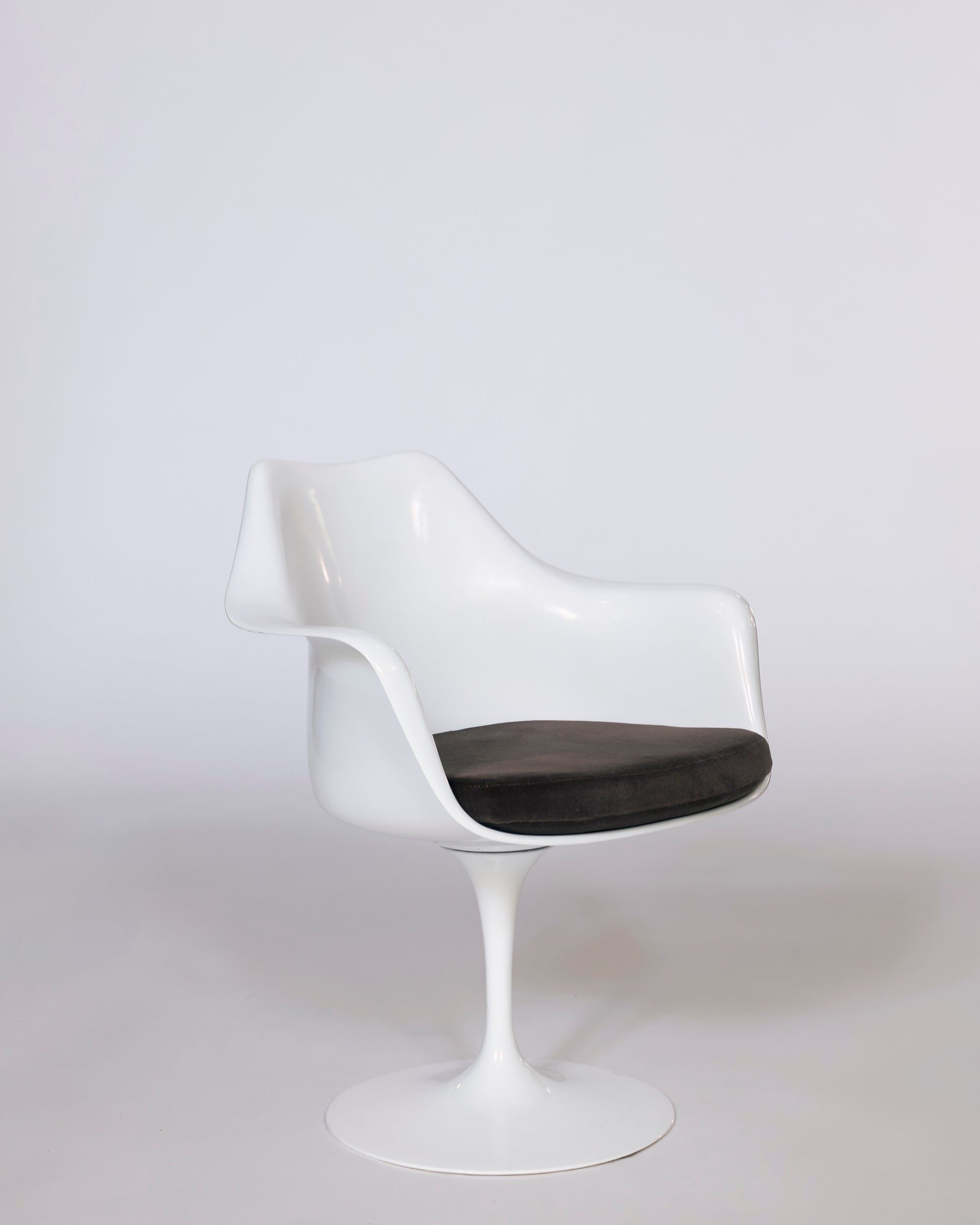The Mid-Century Tulip Armchair features a molded white shell, curved backrest, pedestal base, and black cushioned seat, set against a plain light gray background.
