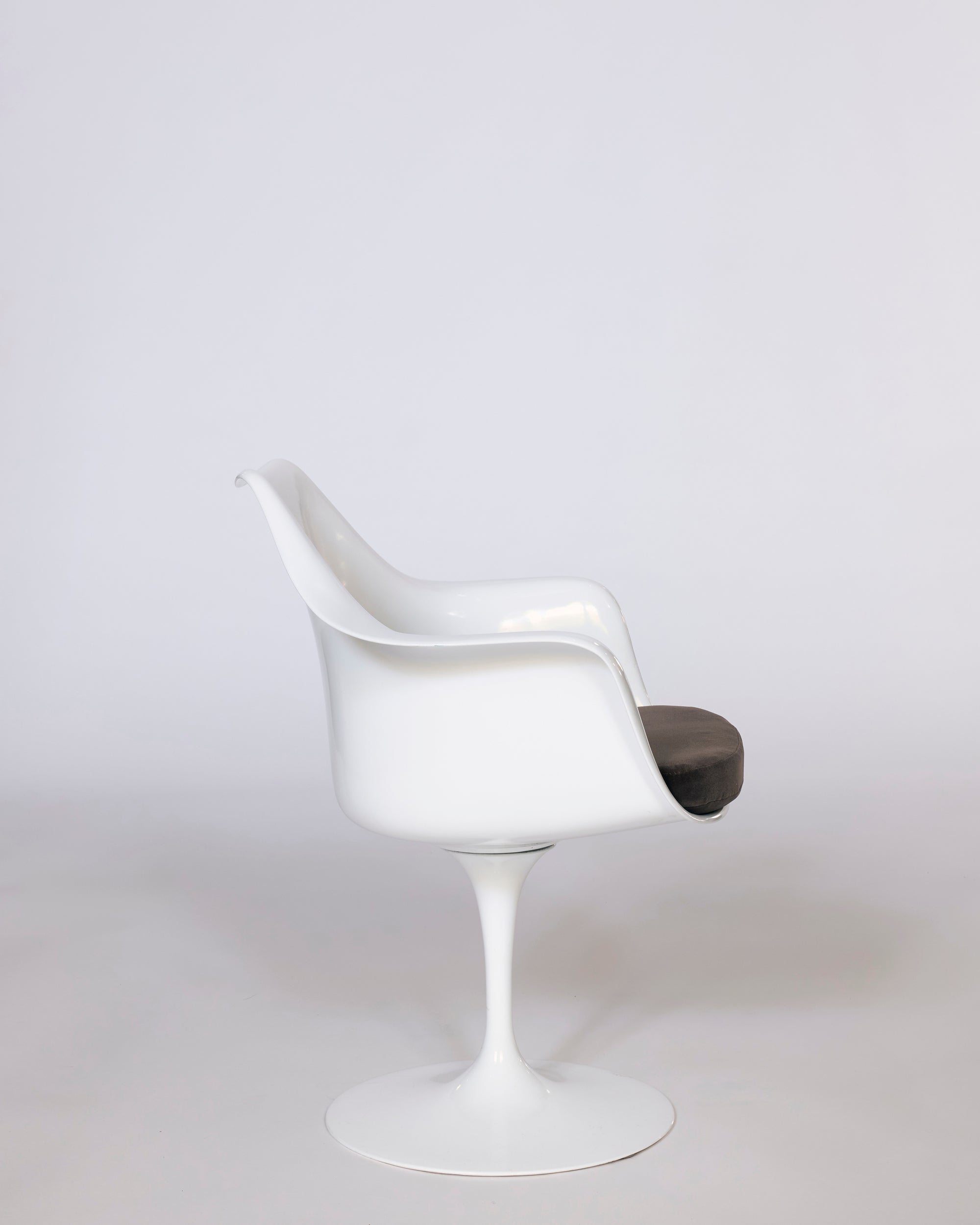 The Mid-Century Tulip Armchair features a molded white shell, curved backrest, single pedestal base, and dark cushioned seat, highlighting modernist design against a plain light background.