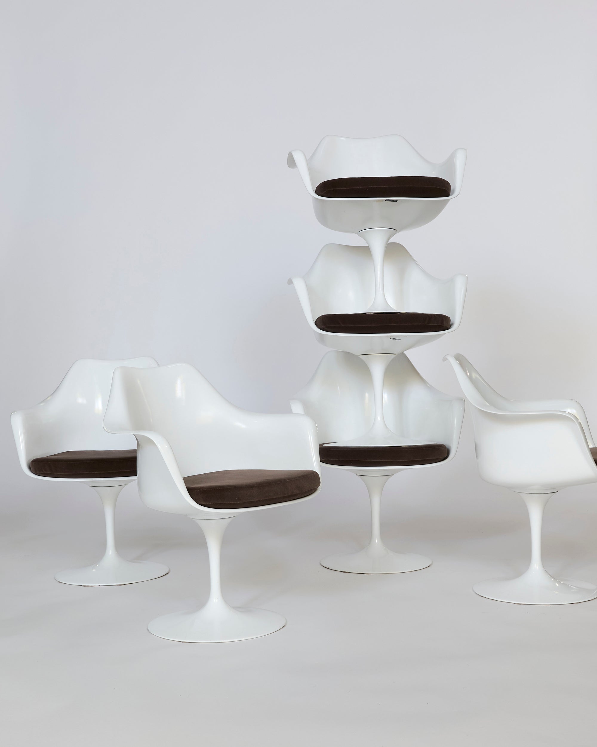 Five Mid-Century Tulip Armchairs with molded white shells and cushioned seats, three on the floor and two stacked, are displayed against a plain white background.