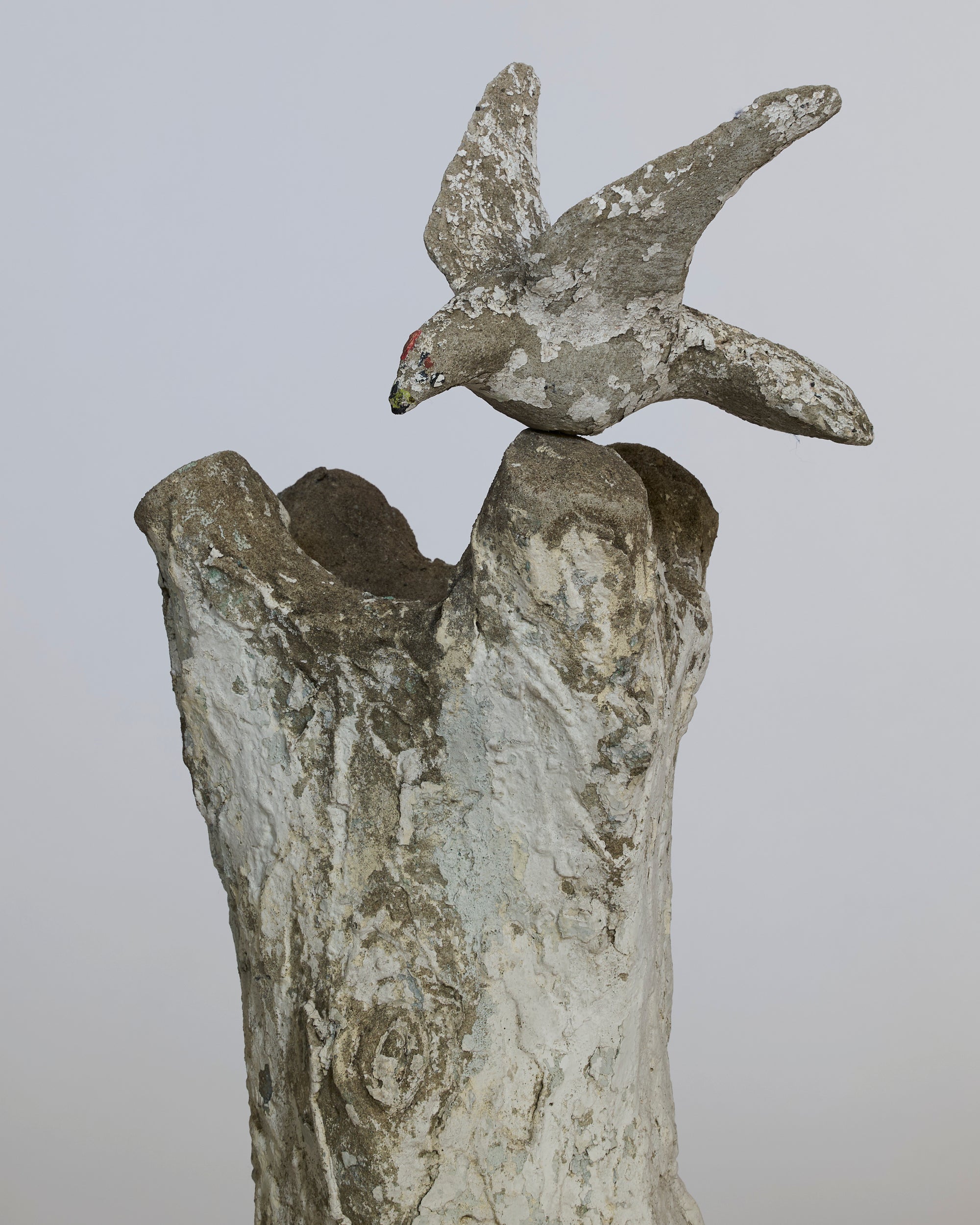 Decorative stone sculpture of a bird perched on a branch against a plain background