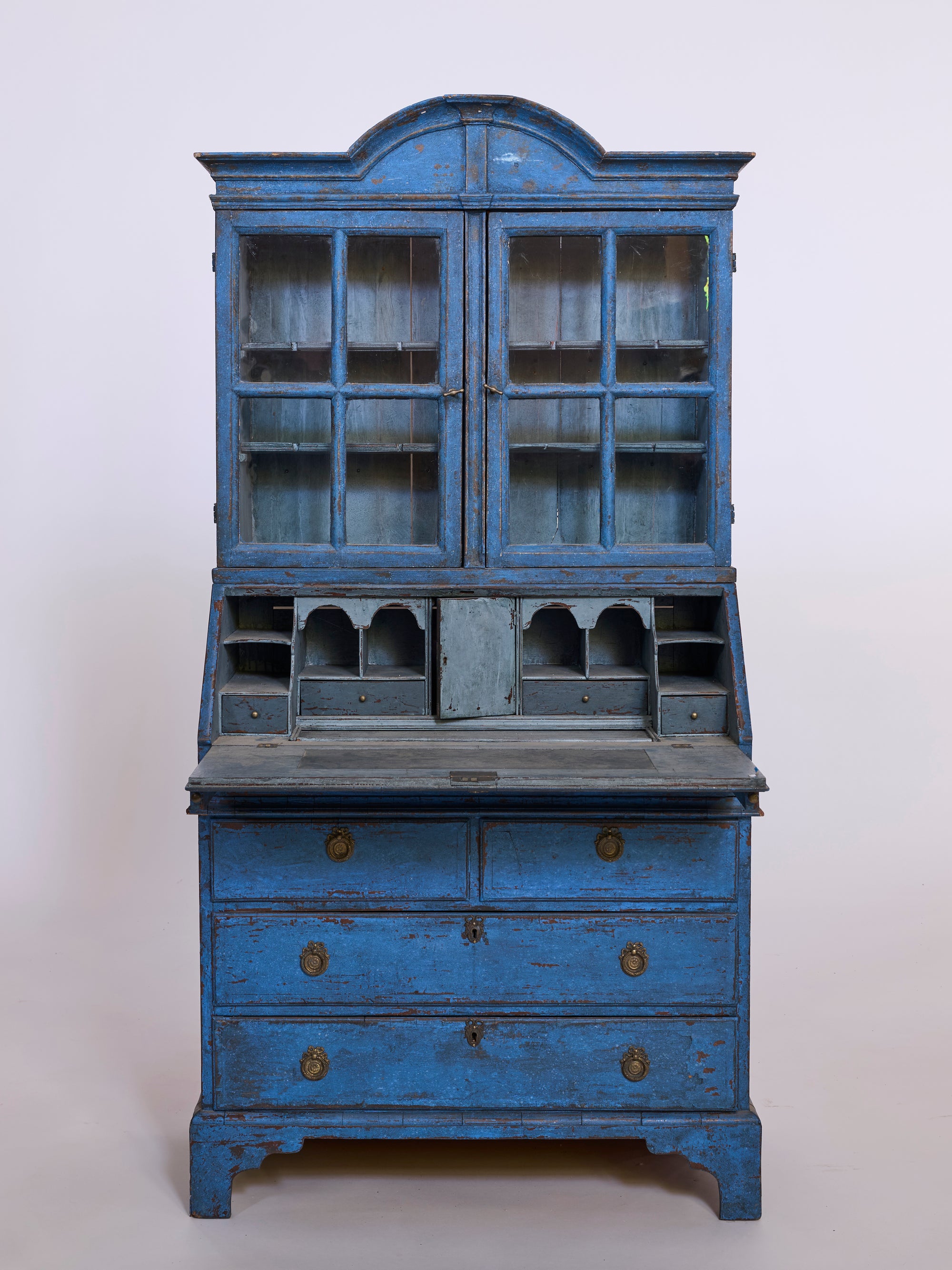 The Antique European Blue Painted Secretary Cabinet with Glass Doors features a fold-down writing surface, small interior drawers, lower storage drawers, and displays charming vintage signs of age and wear.