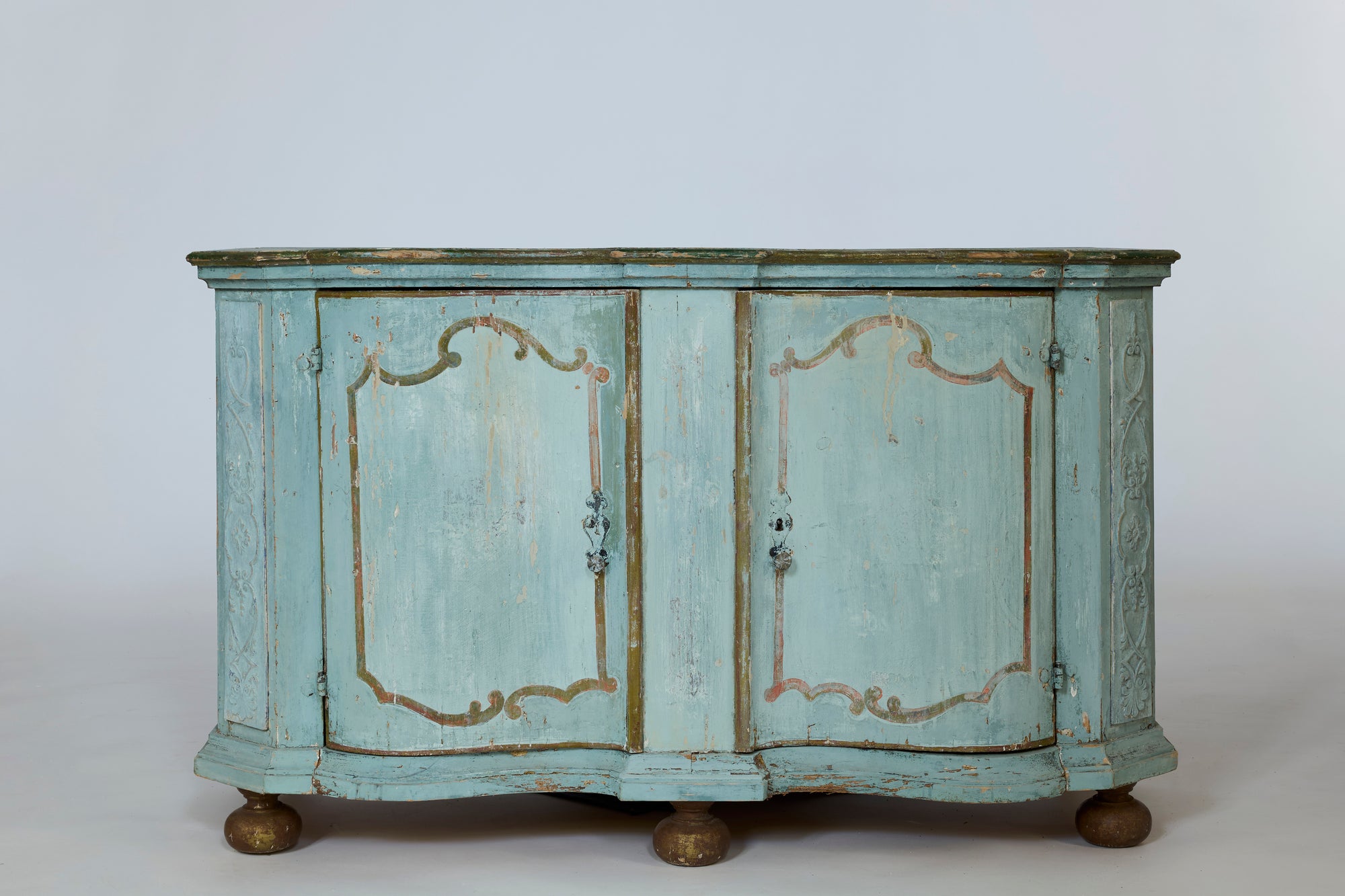 The European Antique Painted Sideboard with Original Patina features vintage light blue wood, ornate detailing, curved edges, hand-painted accents, and round brass feet. Weathered paint reveals hints of blue-green patina against a plain background.