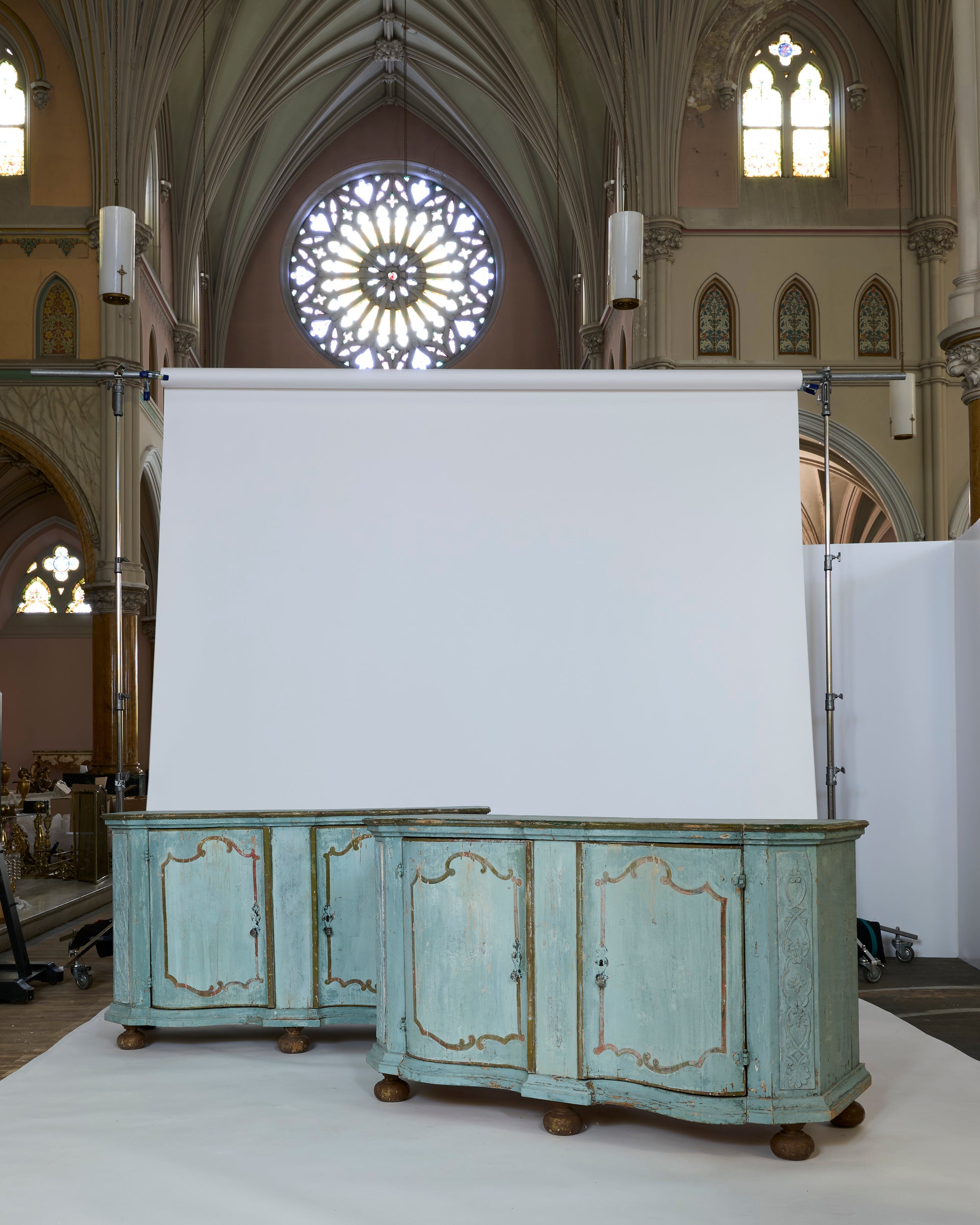 An ornate church interior with stained glass and vaulted ceilings features a European Antique Painted Sideboard with Original Patina in pale blue, placed before a large white photo backdrop.