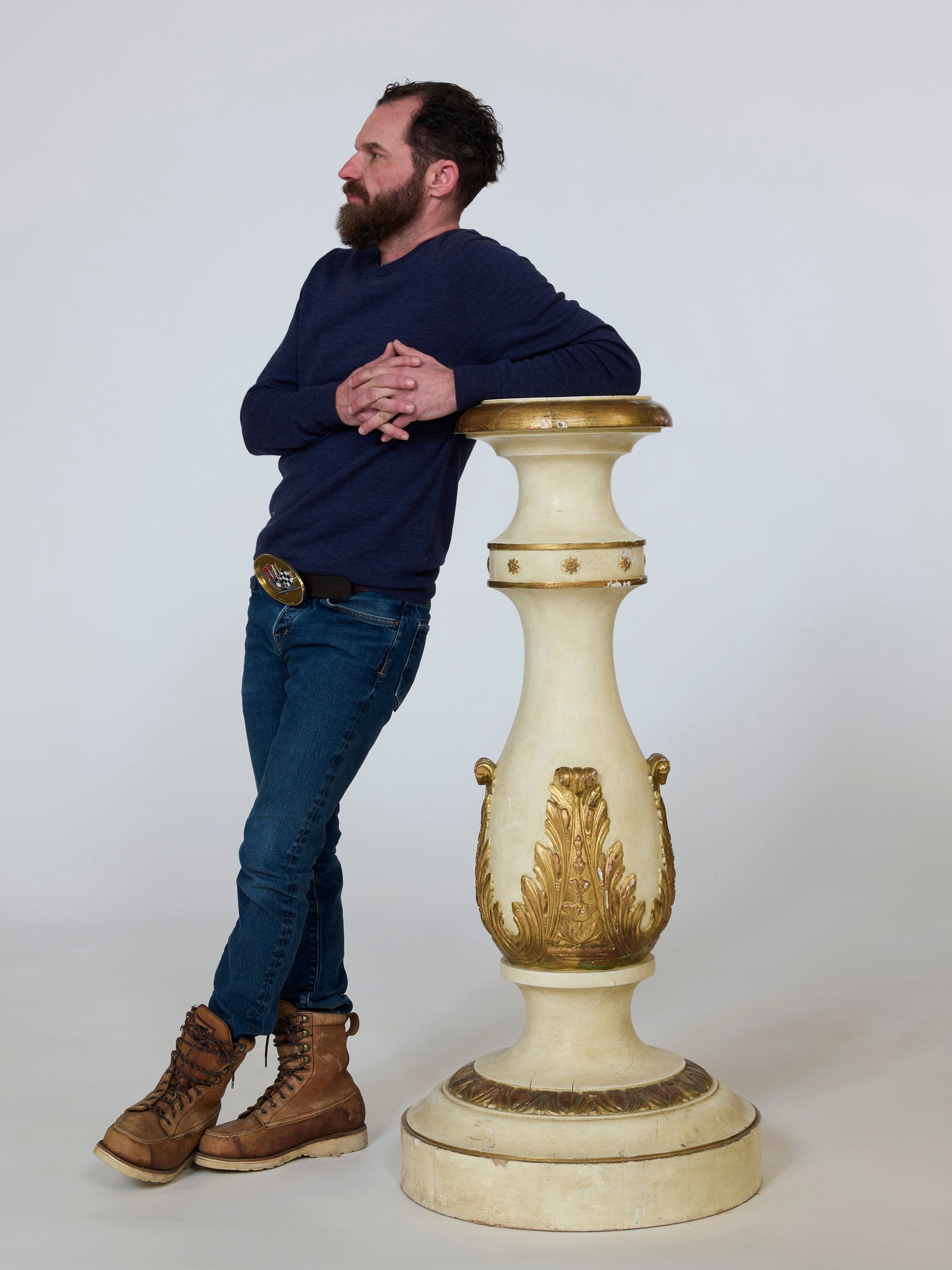 Man leaning against a decorative white and gold pedestal on a plain background