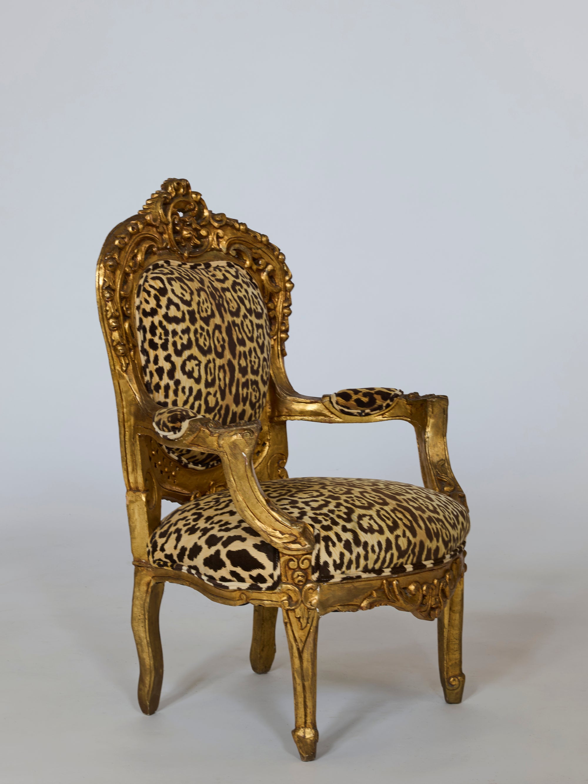 A Pair of Leopard Upholstered Gilt Armchairs with carved baroque frames, featuring intricate detailing and luxurious upholstery, displayed against a plain light gray background.