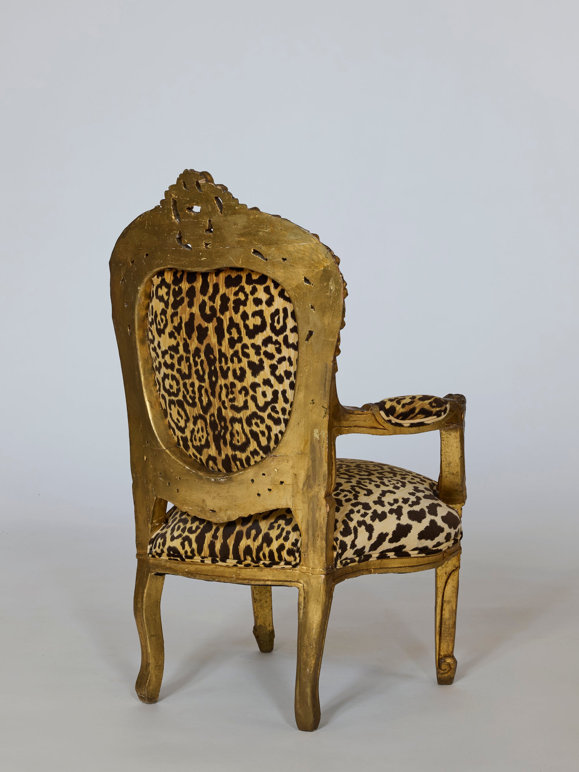 A pair of vintage leopard upholstered gilt armchairs with carved Baroque frames, shown angled from the back on a plain light background.