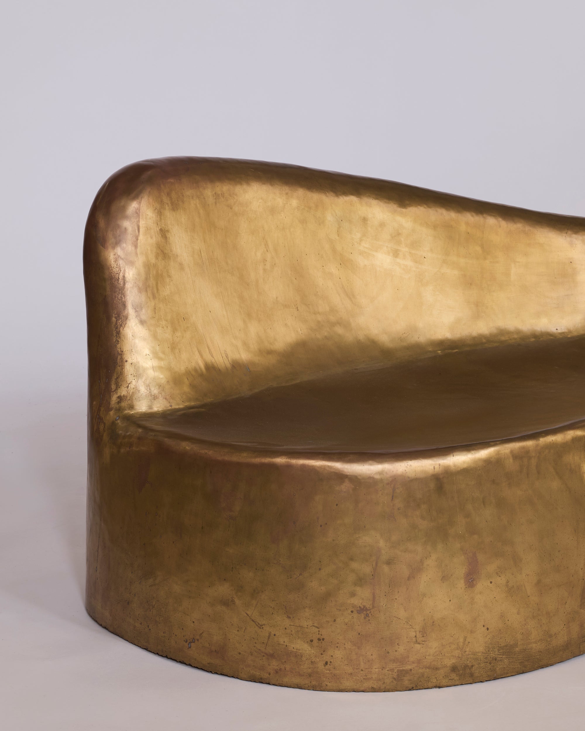 The Sculptural Brass Chaise Lounge features an organic curved form with a smooth, metallic brass finish—an elegant, modern piece of contemporary furniture that doubles as a functional work of art against any light background.