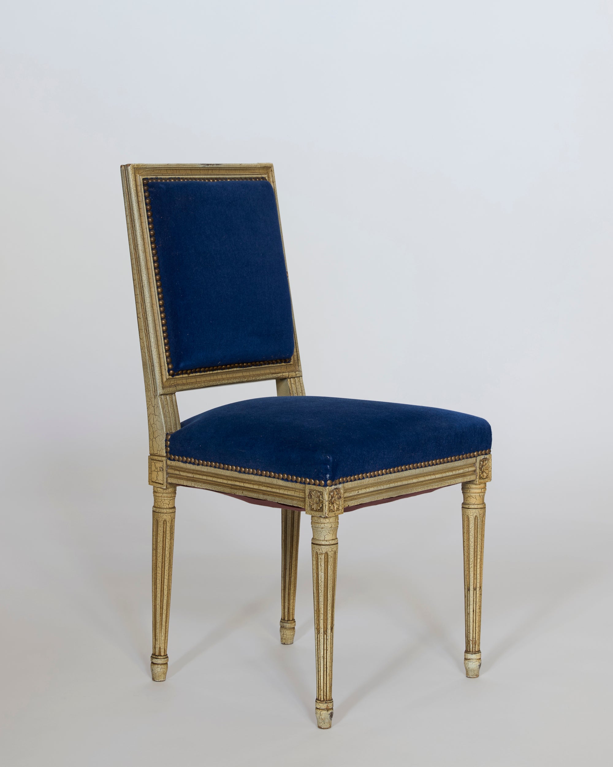 A set of six antique Louis XVI style giltwood chairs with blue velvet upholstery, featuring carved legs and frames, is displayed against a plain light background.