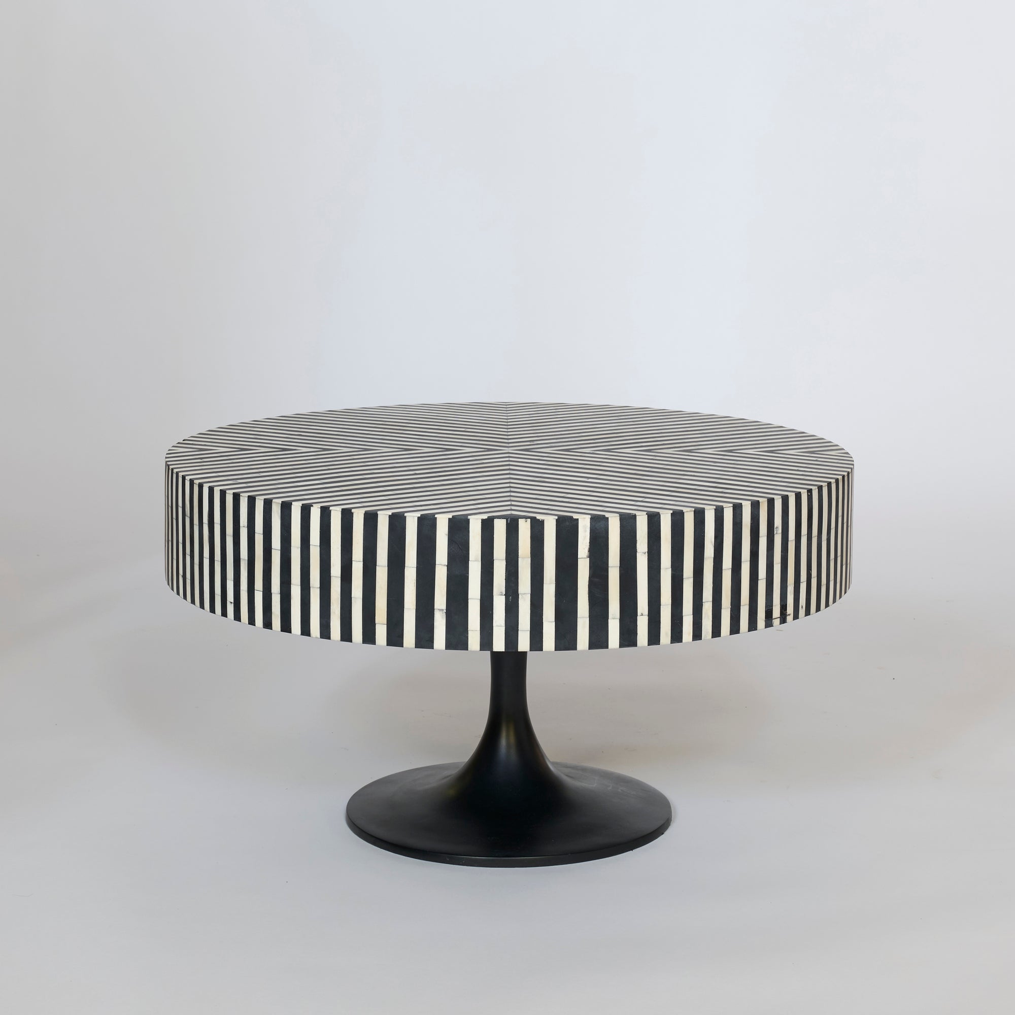 The Black and White Striped Round Coffee Table features a black pedestal base, vertical stripes along the sides, and a grid-patterned round top, all set against a plain light background.