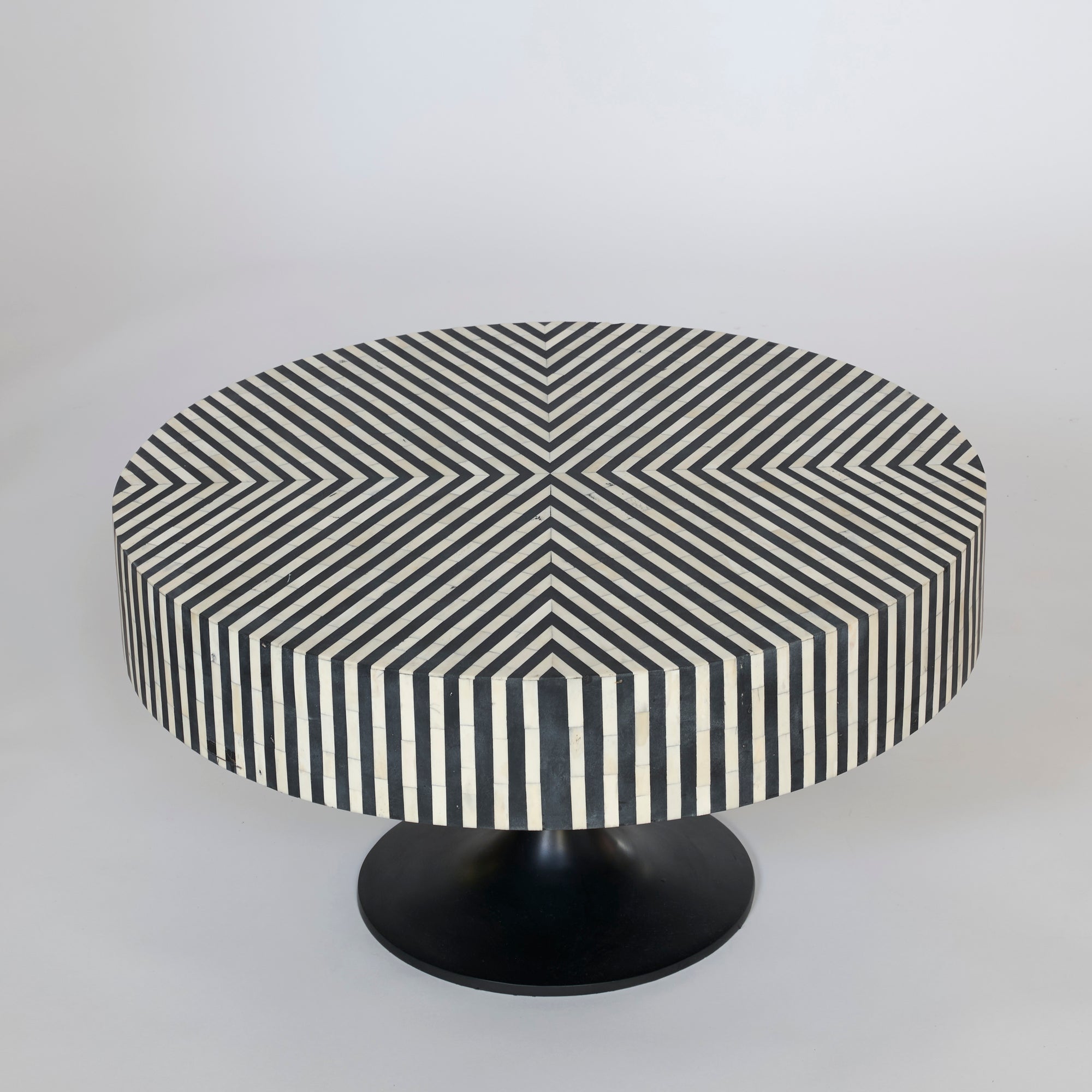 The Black and White Striped Round Coffee Table features a bold geometric pattern on its tabletop and sides, with diagonal lines forming a radiating design that creates a modern optical illusion.