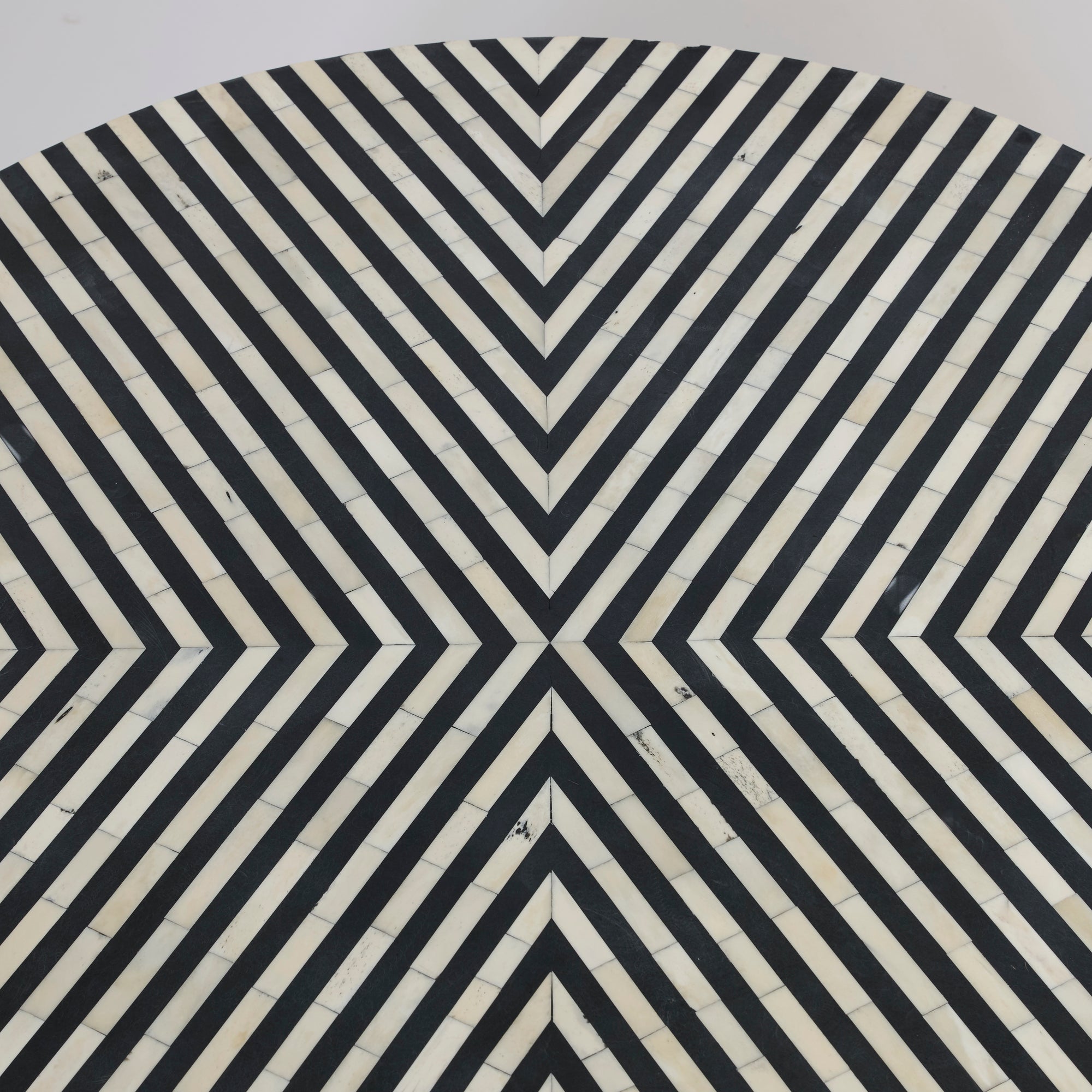 The Black and White Striped Round Coffee Table features concentric chevrons in black and white that meet at the center, creating a bold optical illusion effect and radiating outward in a modern, symmetrical design.