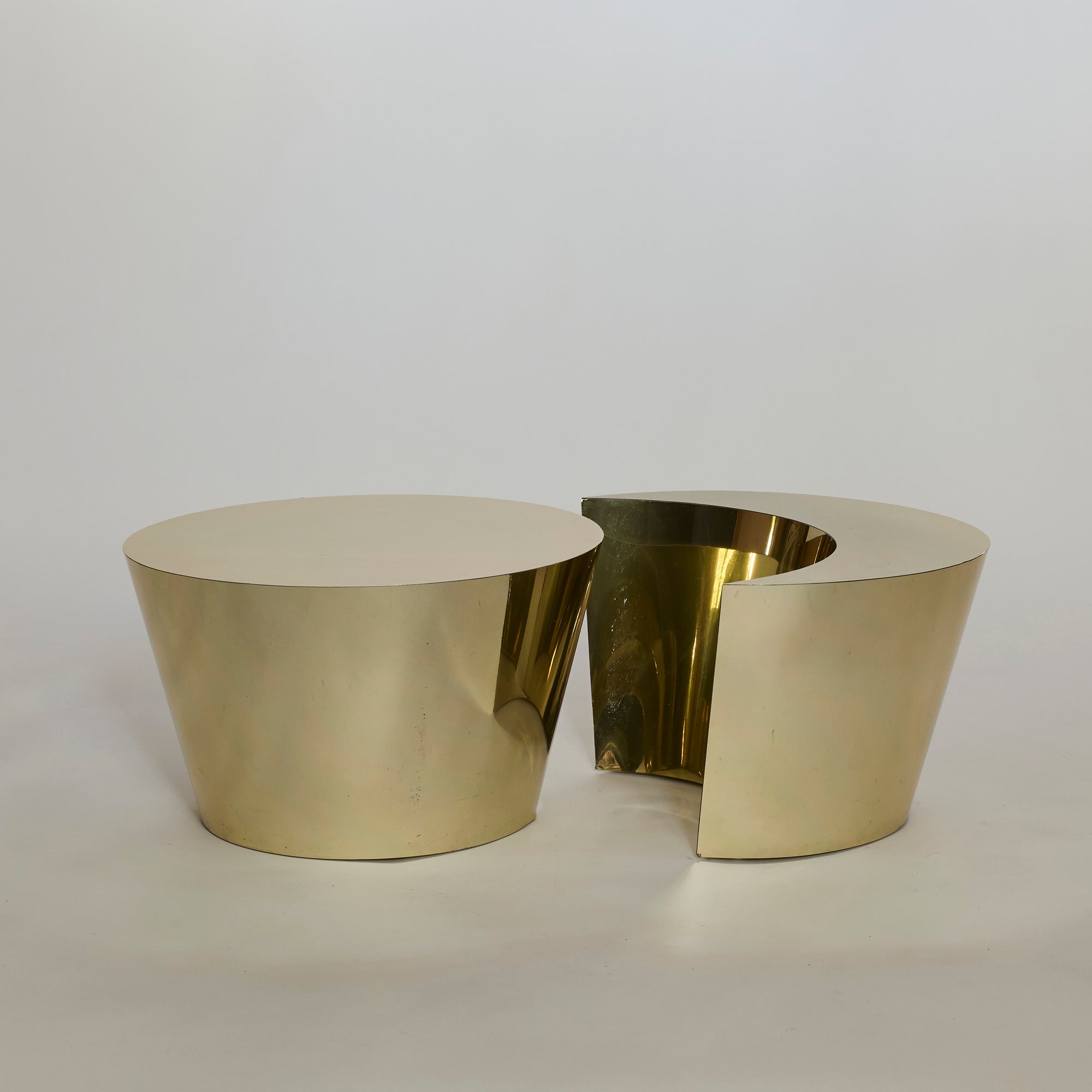 The Laminate Gold Table Set features two shiny, gold, cylindrical tables—one whole and one partially ring-shaped—creating a modern, sculptural coffee table set that stands out against any background.