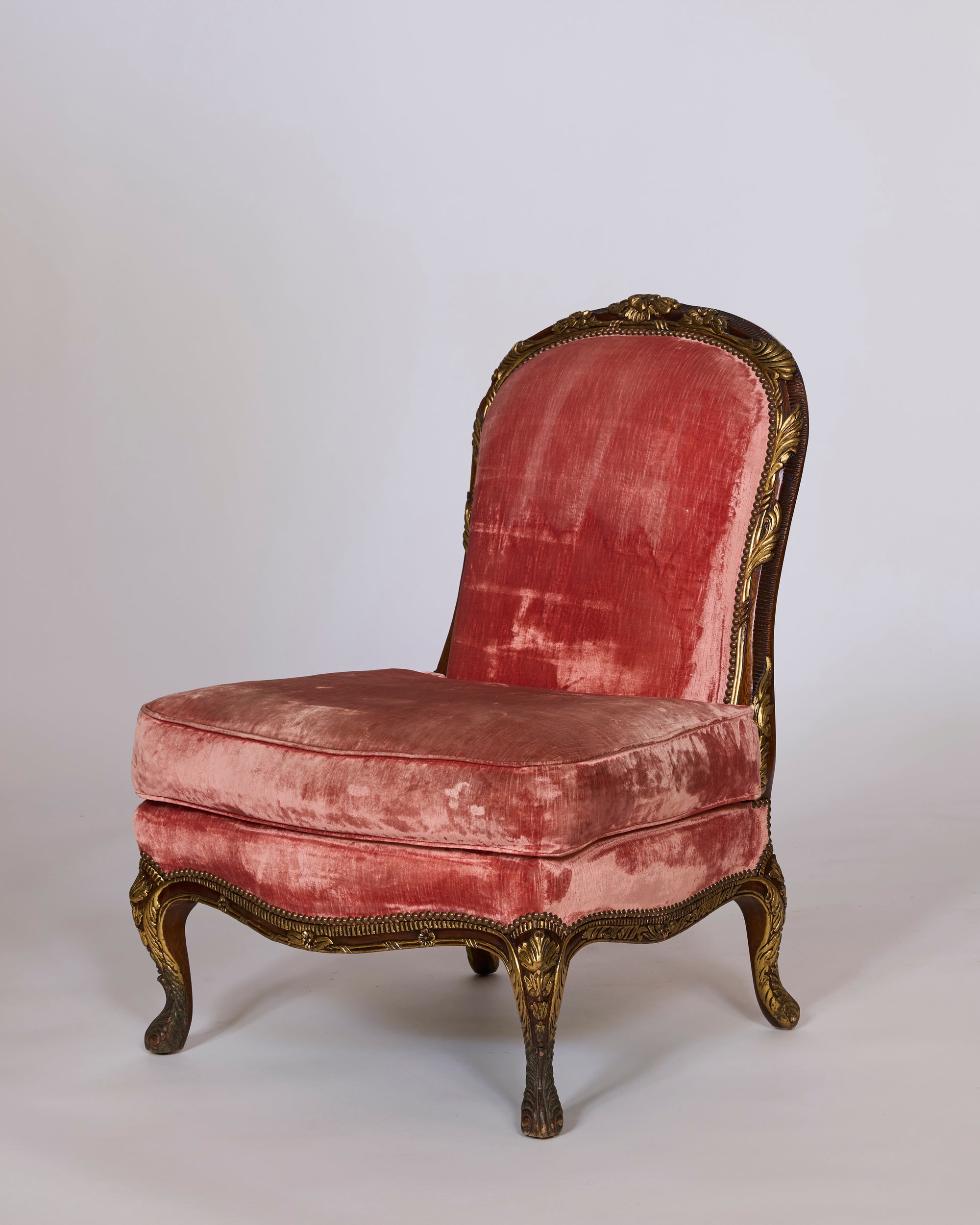 A pair of antique French giltwood slipper chairs with original rose velvet upholstery, showcased against a plain light background.