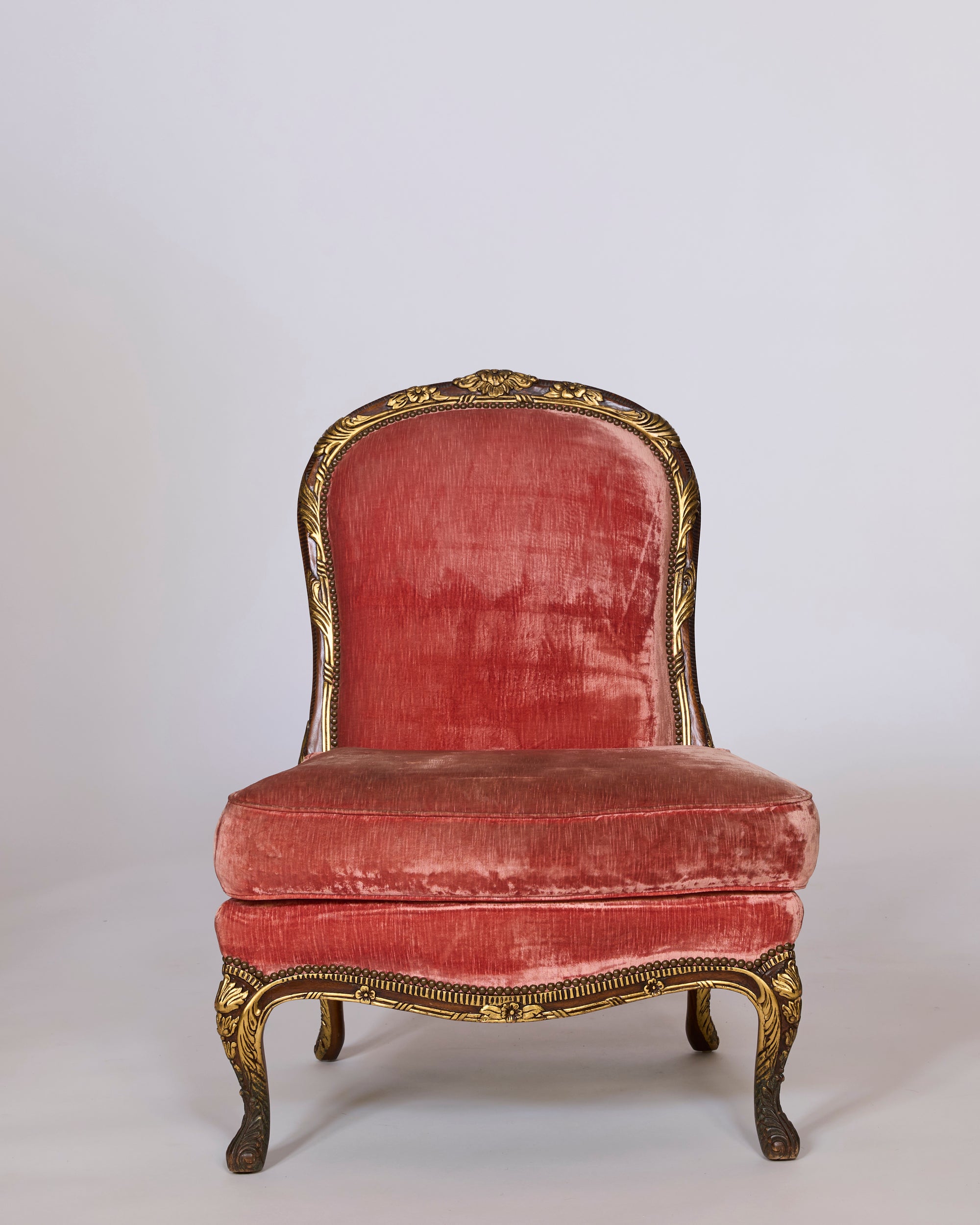 A pair of antique French giltwood slipper chairs with original rose velvet upholstery features ornate frames, curved legs, and rounded backrests, bringing vintage elegance to any space against a plain light background.
