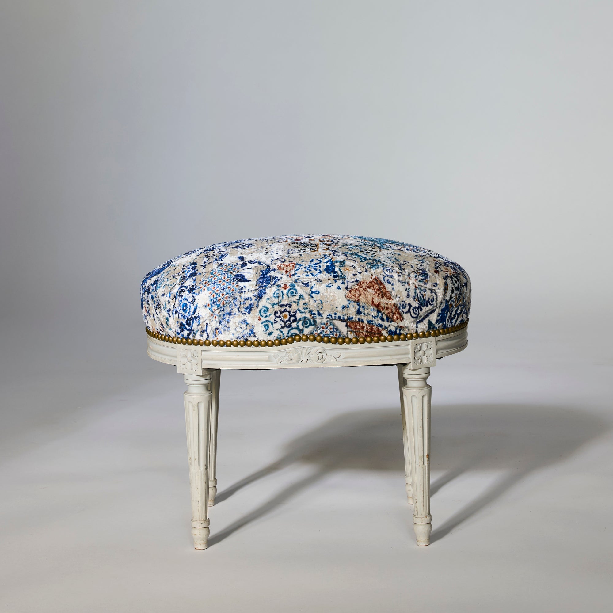 A pair of painted Louis-style stools with carved wooden bases and legs, featuring distressed blue and cream upholstered seats for a touch of European elegance.
