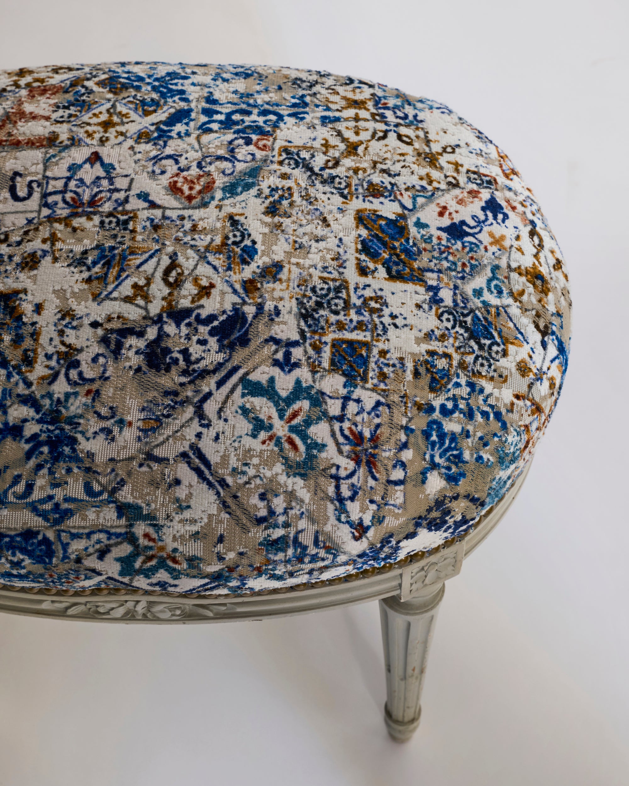 A close-up of a pair of painted Louis-style stools, featuring distressed blue and cream upholstery that highlights their refined details and European elegance.