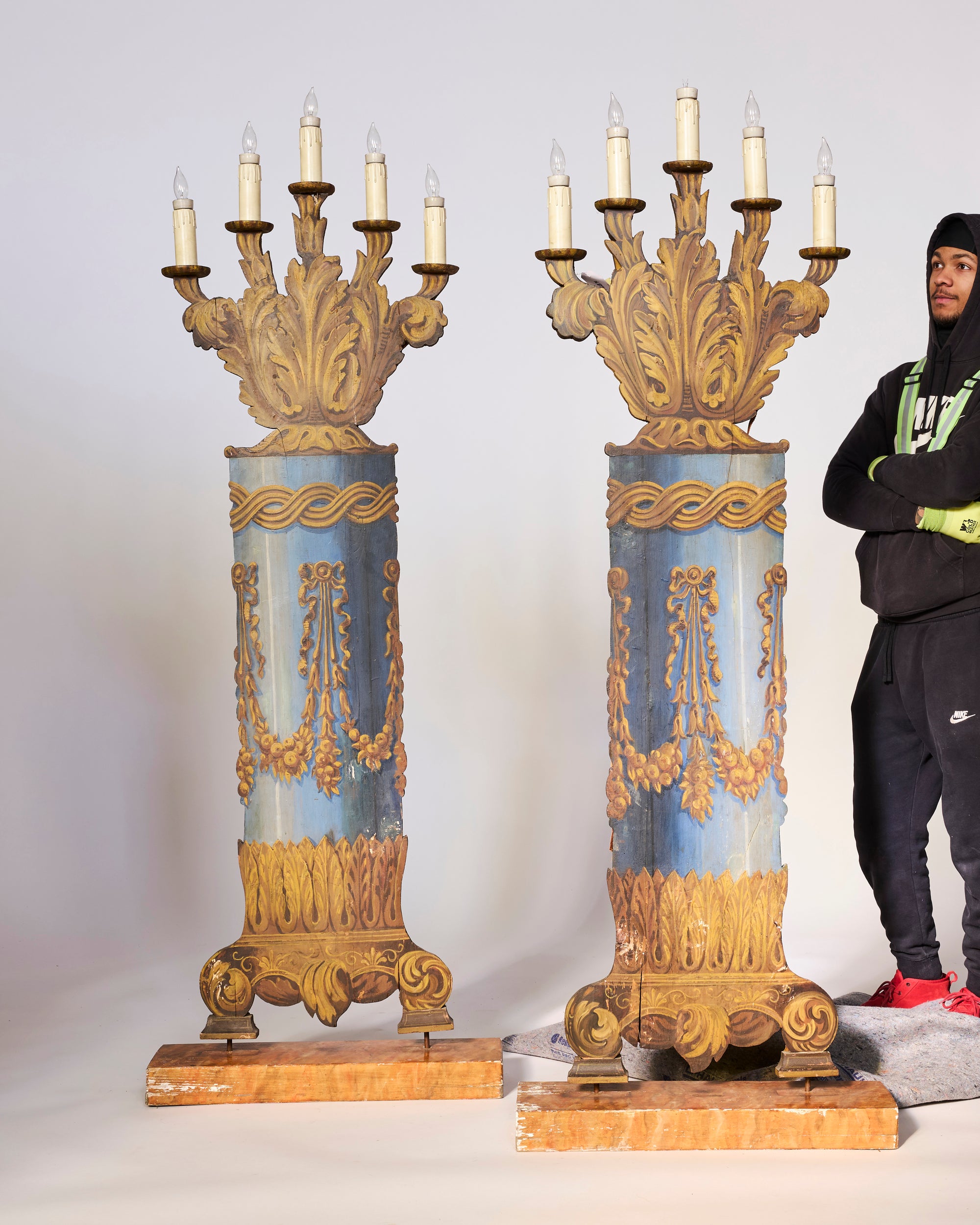 A person in black stands beside a Pair of Antique Opera House Stage Candelabra—large, ornate blue and gold pieces with candle-shaped lights—highlighting the monumental scale of these stunning antique sculptures.