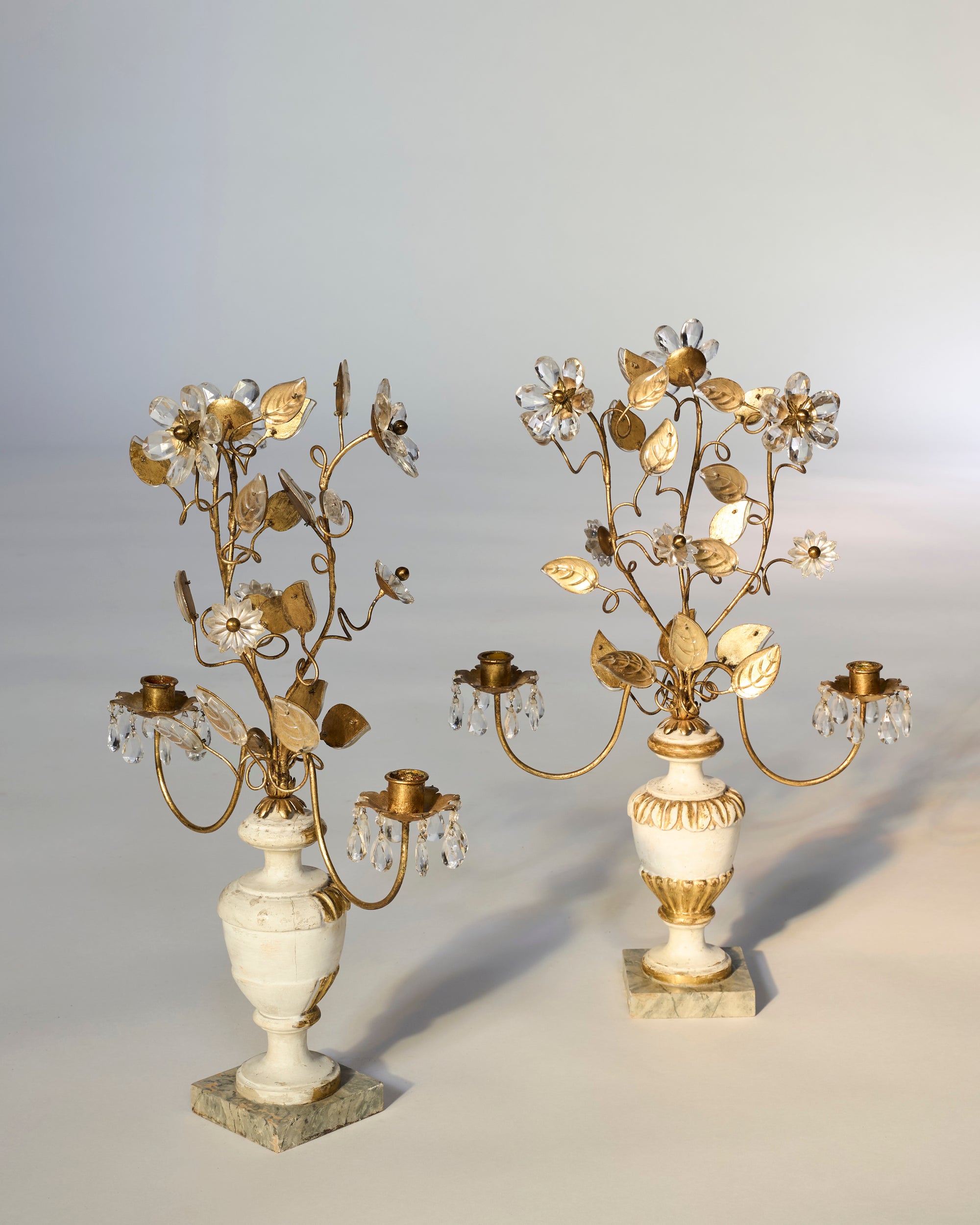 A Pair of Floral Gilt Candelabra with Crystal Drops on Marble Bases features gold branches, leaf and flower accents, and three candle holders each—ideal for European décor. Displayed against a neutral background.