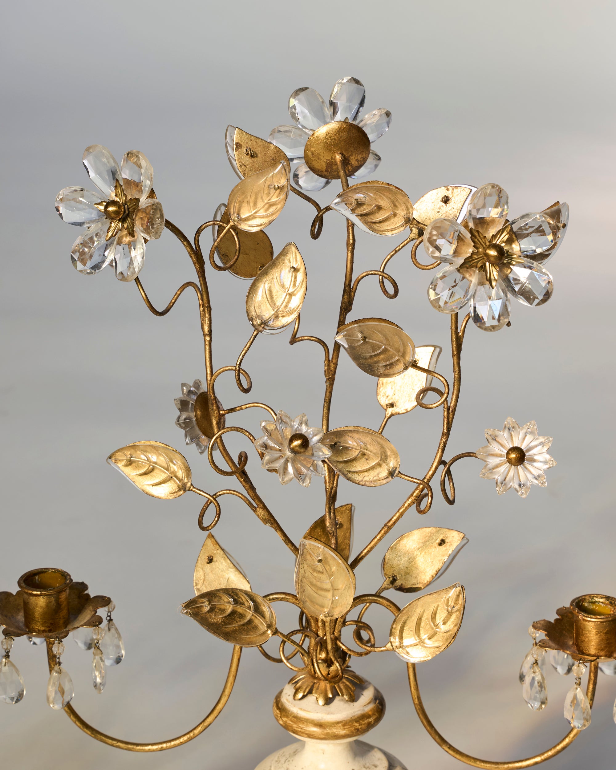 The Pair of Floral Gilt Candelabra with Crystal Drops on Marble Bases features two candle holders, ornate leaves, and crystal accents, bringing sophisticated European elegance to your décor against a softly blurred background.