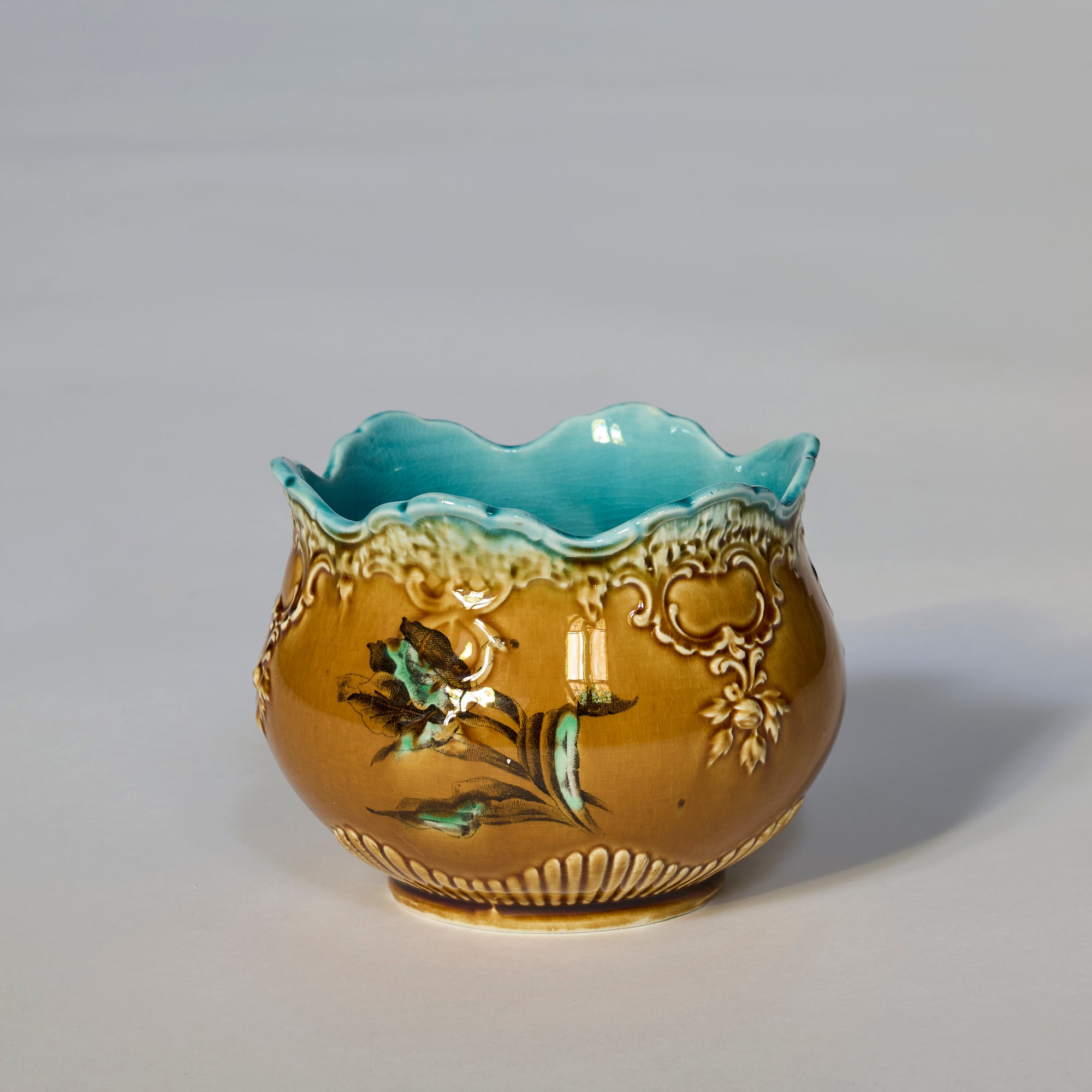 The Antique Majolica Style Floral Cachepot features a scalloped rim, turquoise interior, and embossed hand-painted floral motifs with painted flowers, set against a plain light background.