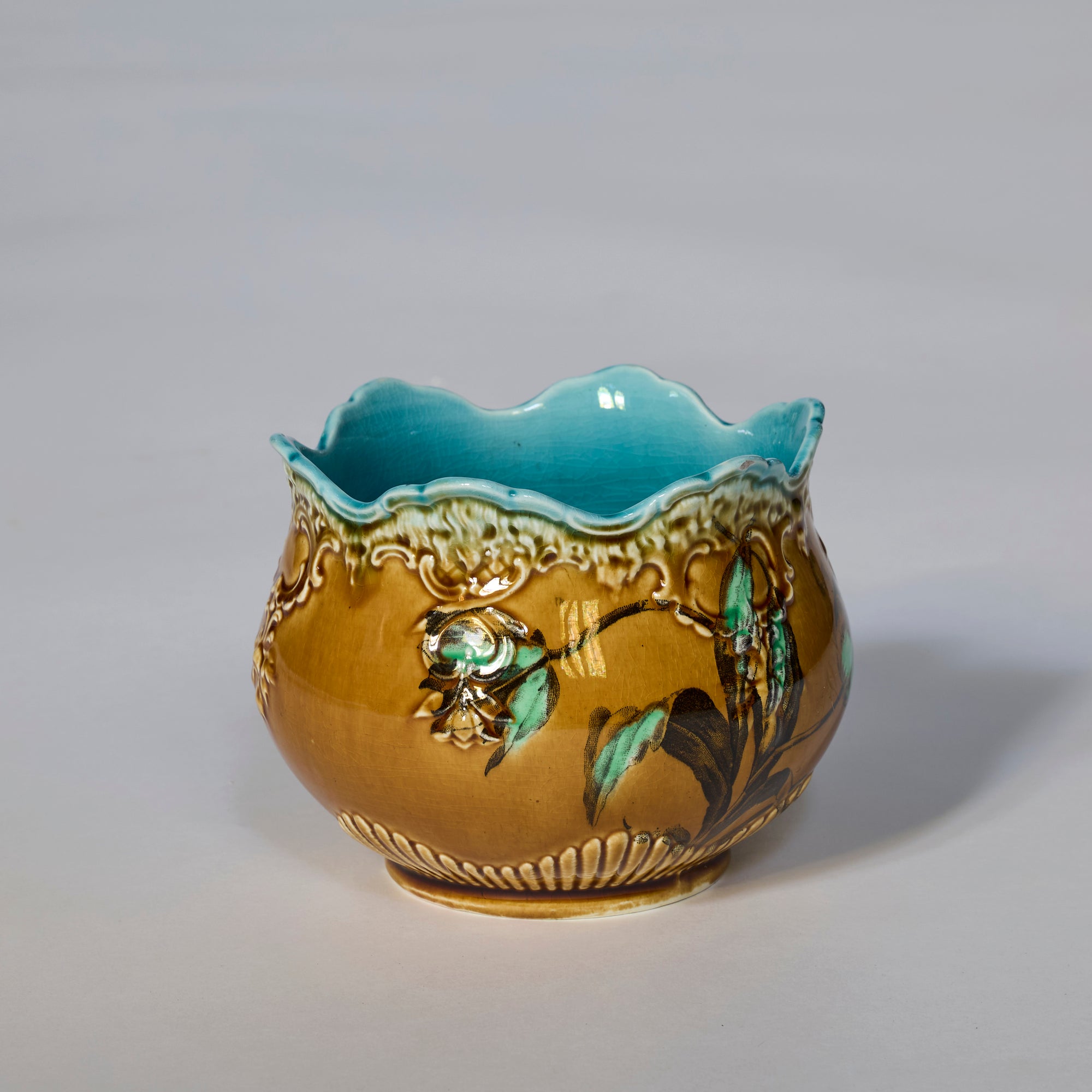 The Antique Majolica Style Floral Cachepot with Scalloped Rim features hand-painted blue, green, and cream floral motifs, a glazed turquoise interior, brown exterior, and an elegant scalloped rim for a vintage decorative touch.