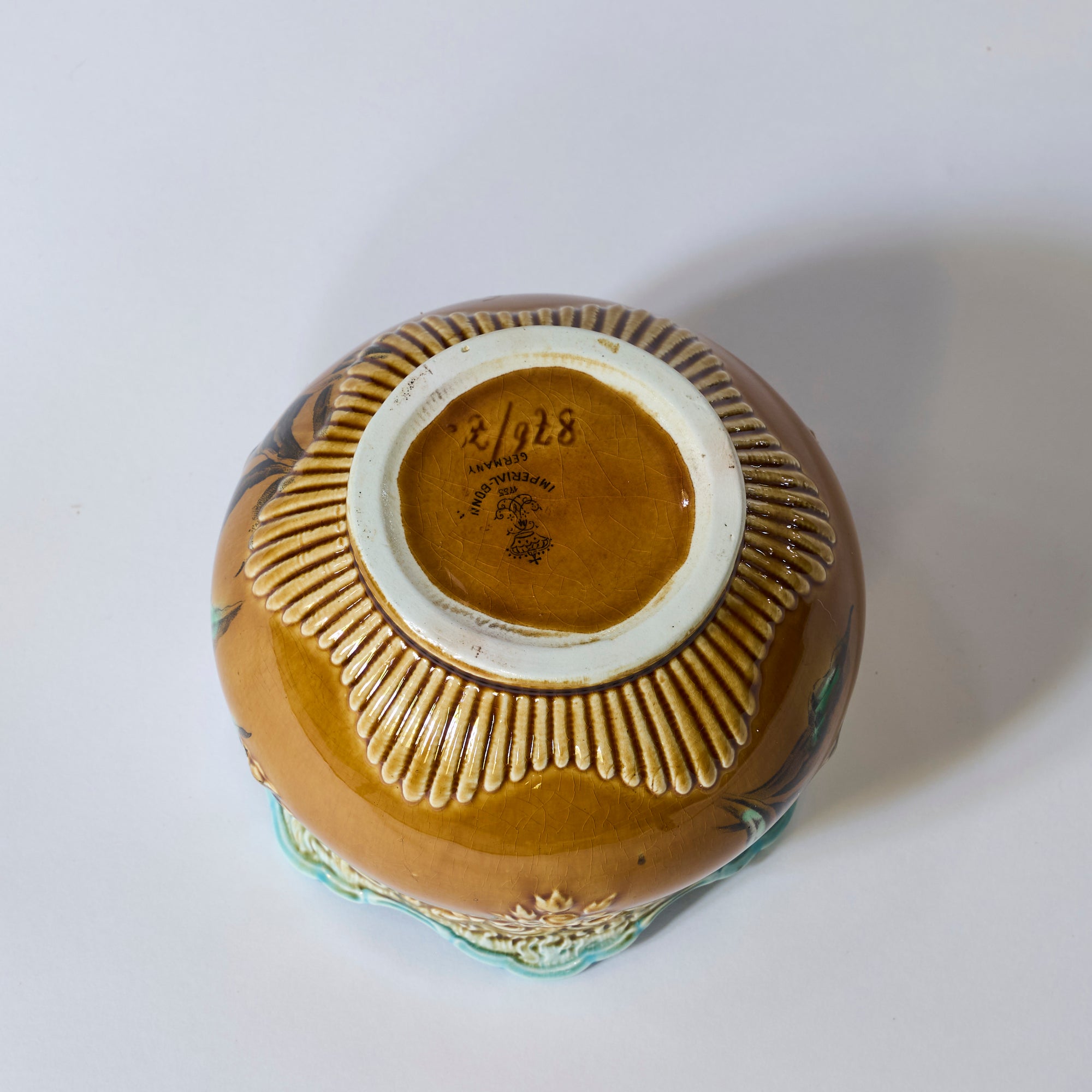 The Antique Majolica Style Floral Cachepot with Scalloped Rim is displayed upside down, showing its brown base with a ring of raised ridges and a maker’s mark on the bottom, all set against a plain white background.