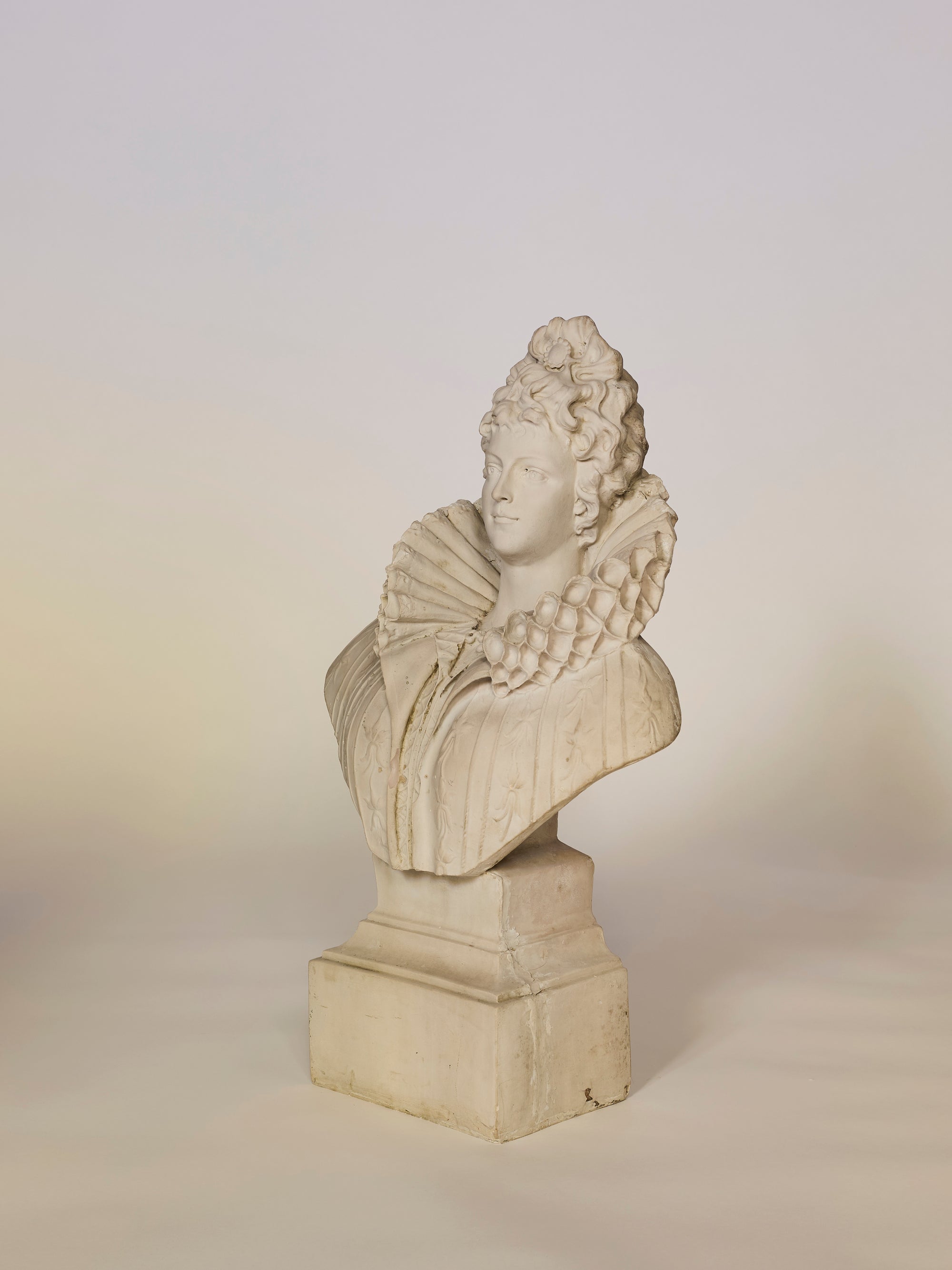 Statue of a classical bust on a pedestal against a plain background