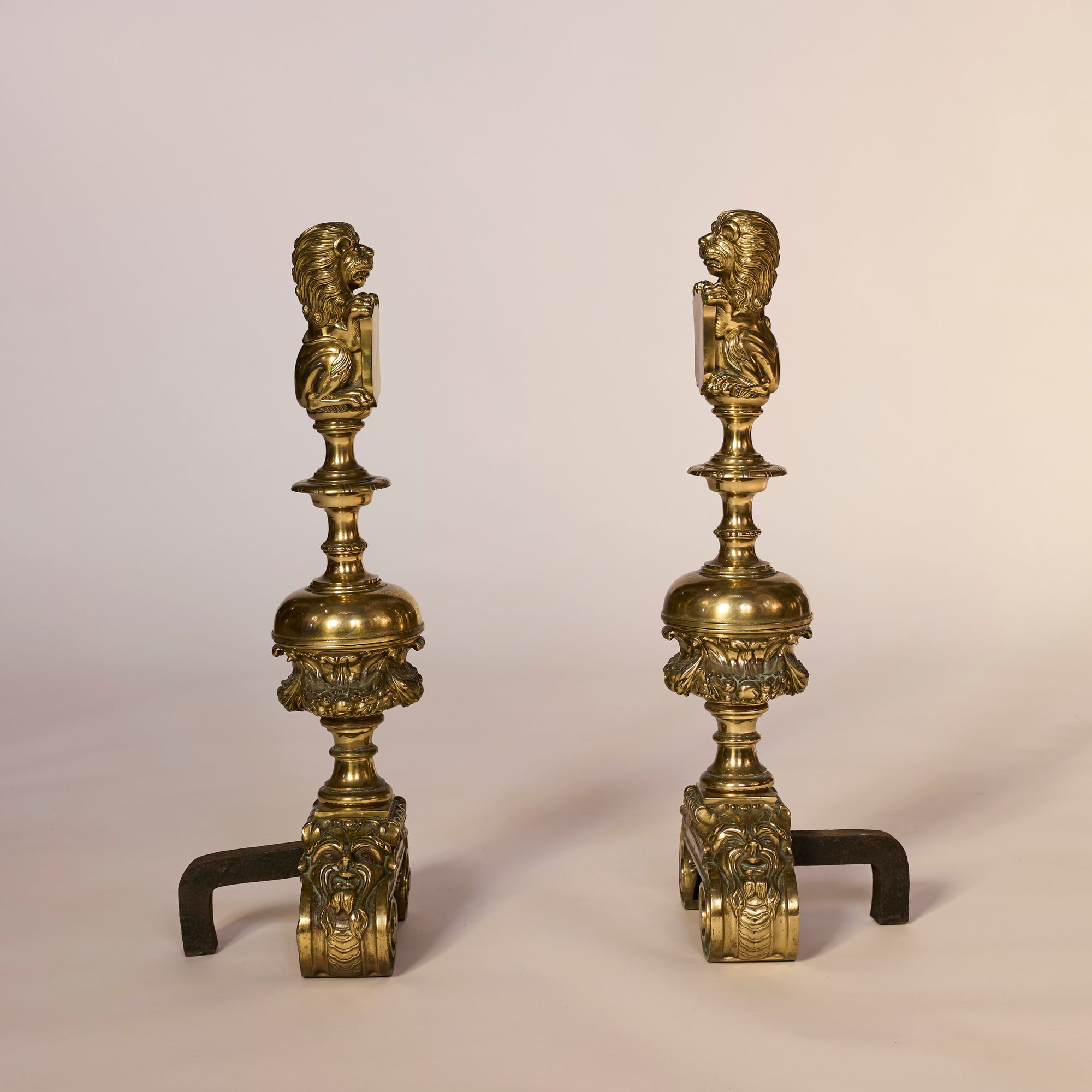 Pair of ornate brass candle holders with classical designs on a beige background