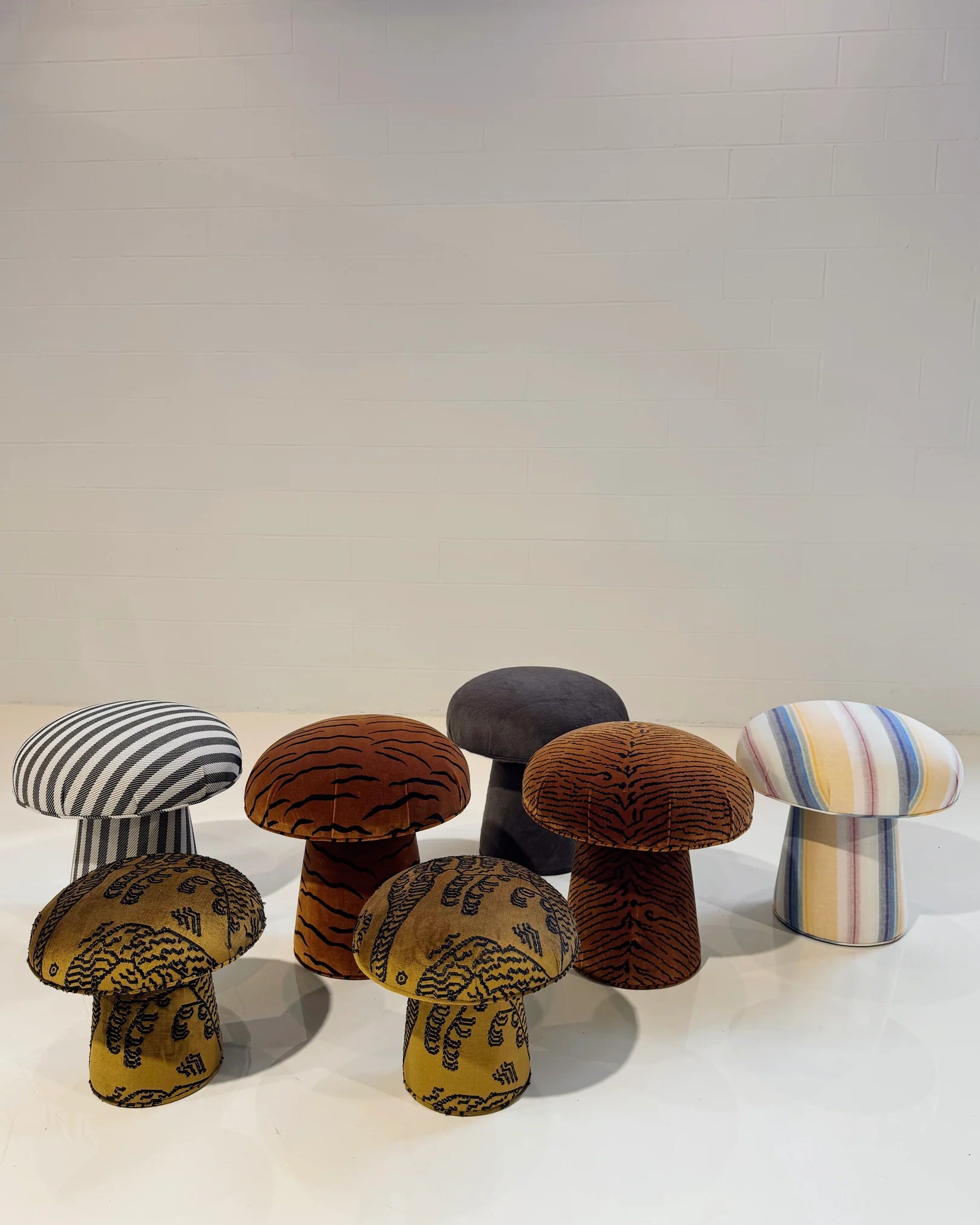 Six Forsyth Mushroom Poufs in Dedar 'This Is The Tiger Speaking' jacquard velvet, featuring tiger stripes and bold patterns in black and grey, are arranged on a white floor against a plain, light-colored wall.